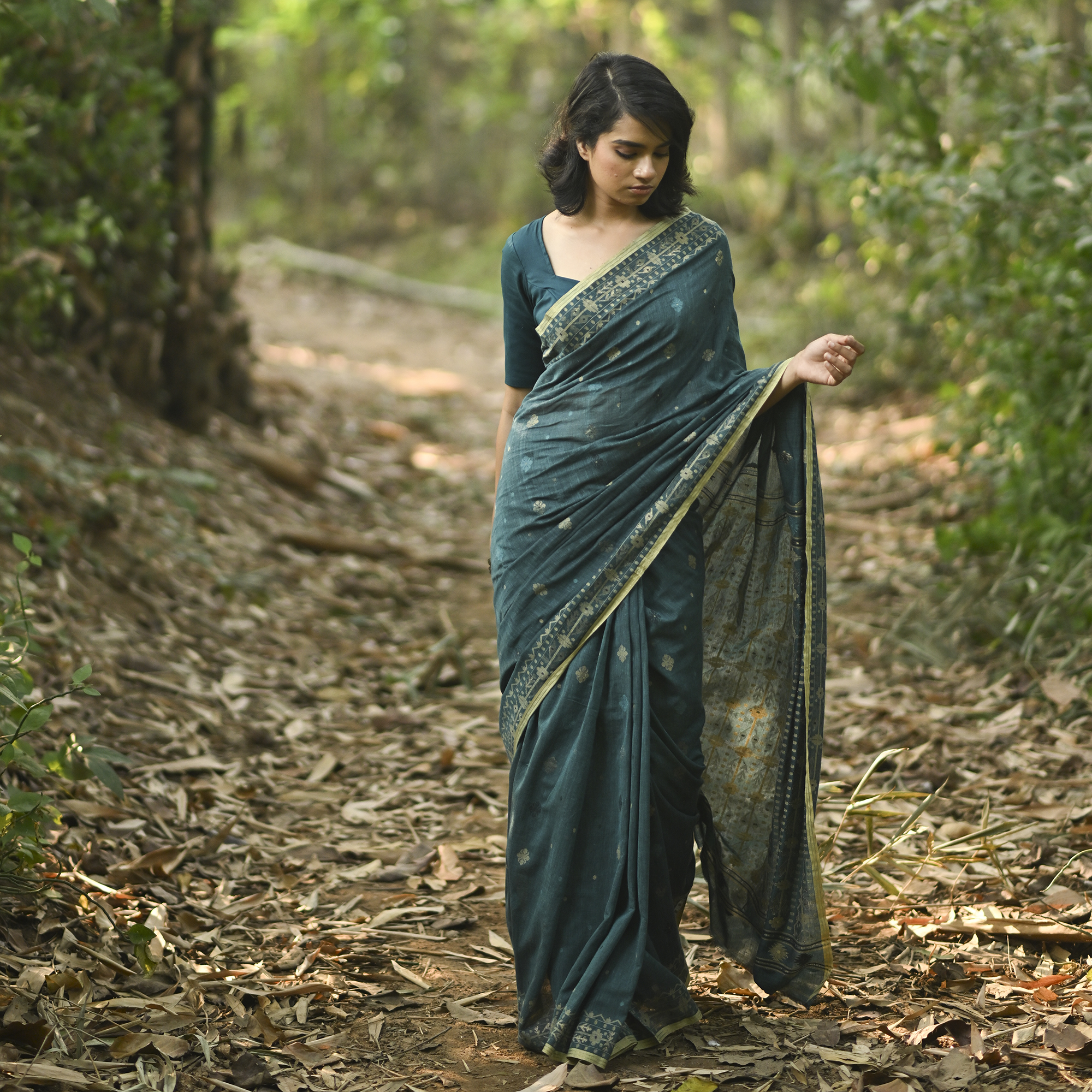 Model wearing the Teal Antique-Gold Jamdani Saree, a handwoven deep teal with antique-gold weaving Jamdani saree with fine woven motifs and classic border detailing and intricately woven pallu with festive sheen.