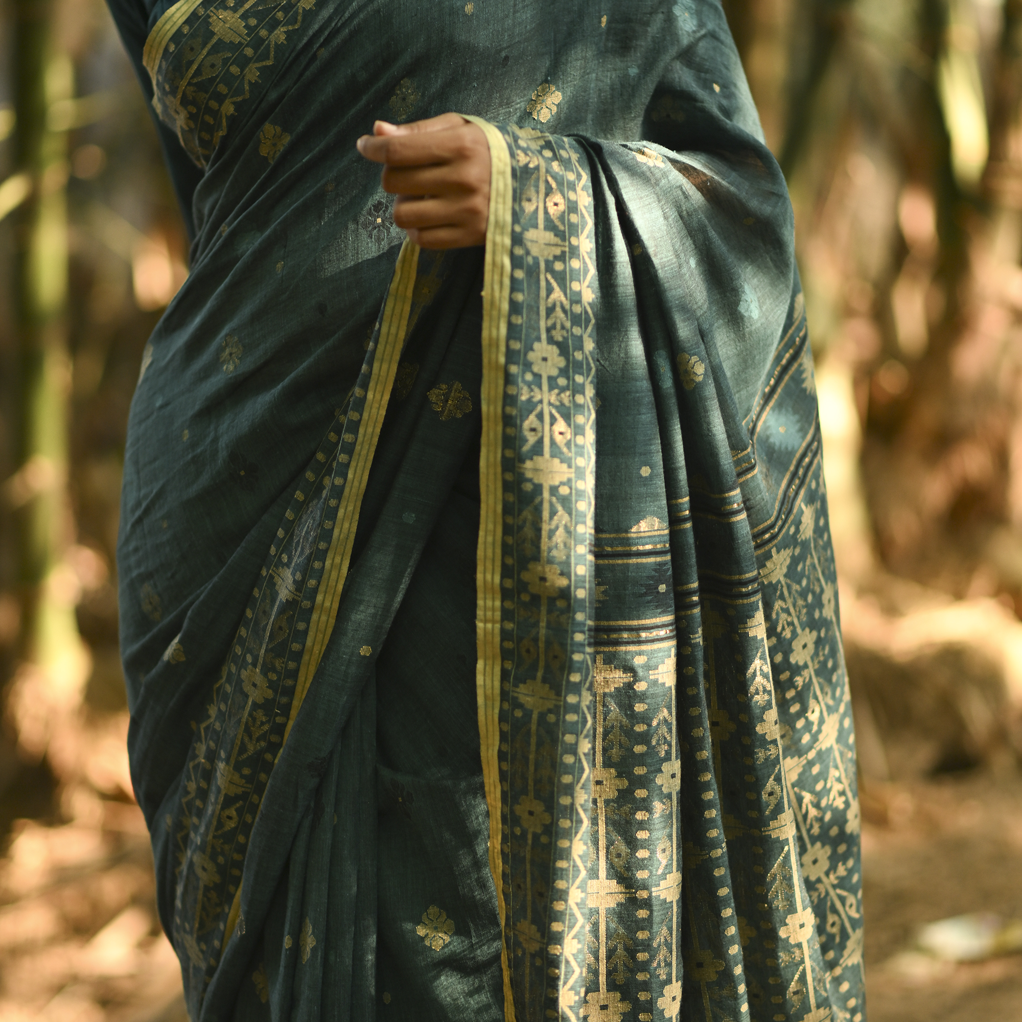 Model wearing the Teal Antique-Gold Jamdani Saree, a handwoven deep teal with antique-gold weaving Jamdani saree with fine woven motifs and classic border detailing and intricately woven pallu with festive sheen.