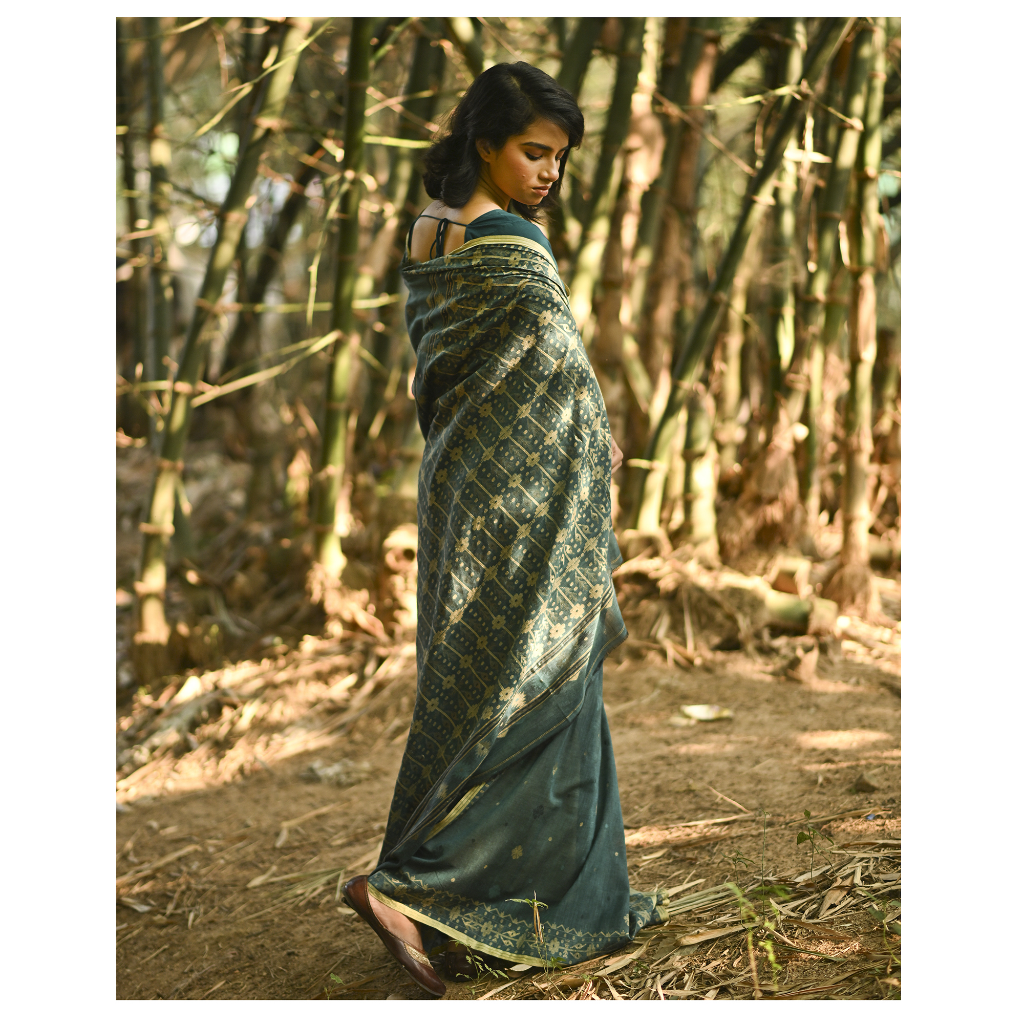 Model wearing the Teal Antique-Gold Jamdani Saree, a handwoven deep teal with antique-gold weaving Jamdani saree with fine woven motifs and classic border detailing and intricately woven pallu with festive sheen.