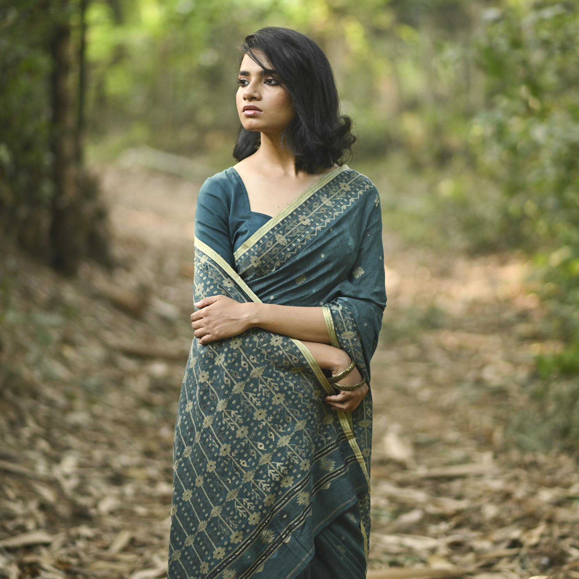 Model wearing the Teal Antique-Gold Jamdani Saree, a handwoven deep teal with antique-gold weaving Jamdani saree with fine woven motifs and classic border detailing and intricately woven pallu with festive sheen.