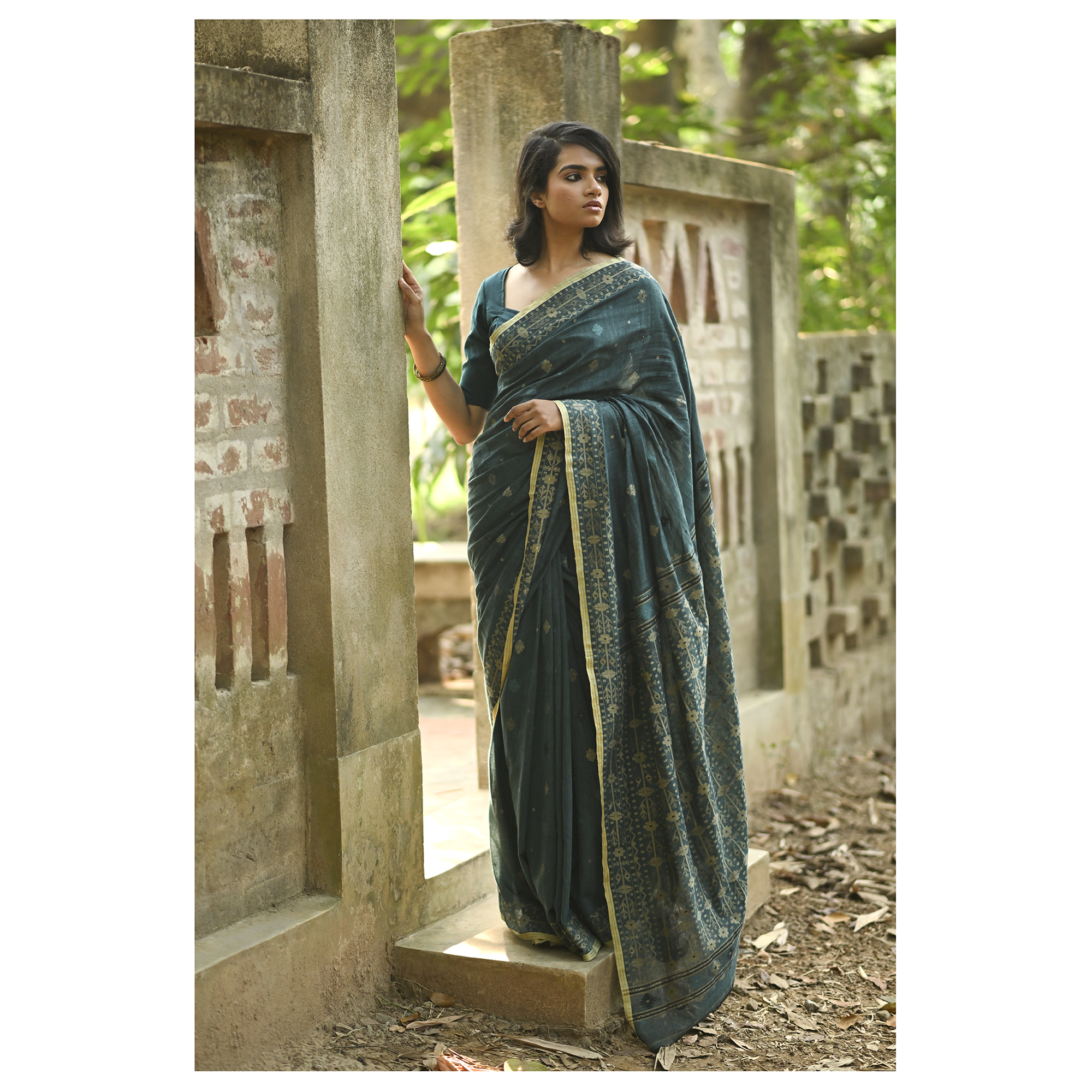 Model wearing the Teal Antique-Gold Jamdani Saree, a handwoven deep teal with antique-gold weaving Jamdani saree with fine woven motifs and classic border detailing and intricately woven pallu with festive sheen.