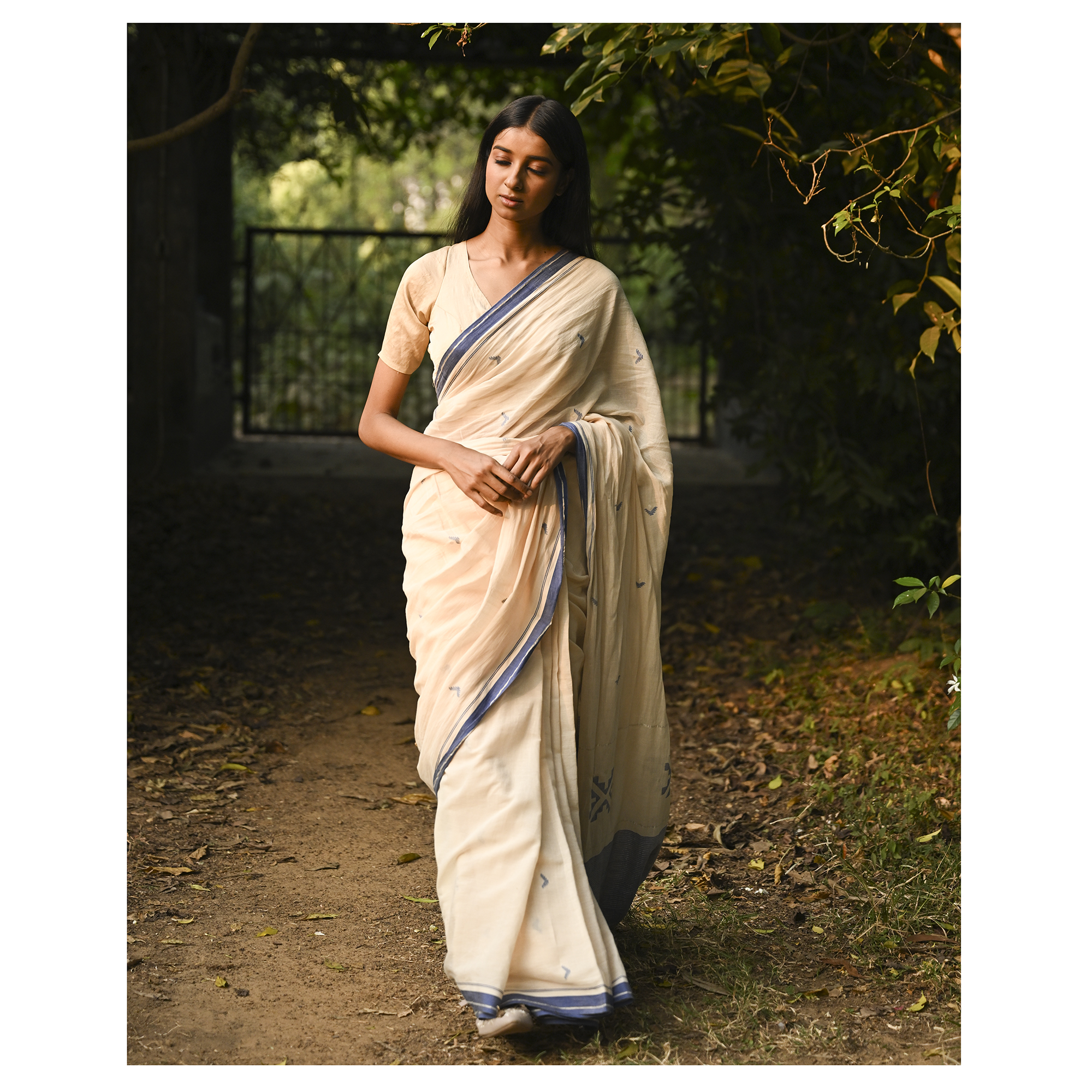 Model wearing the Ivory Blue-Border Jamdani Saree, a handwoven soft ivory with muted blue border accents Jamdani saree with minimal woven accents with quiet buti work and clean pallu framed by a restrained blue border.