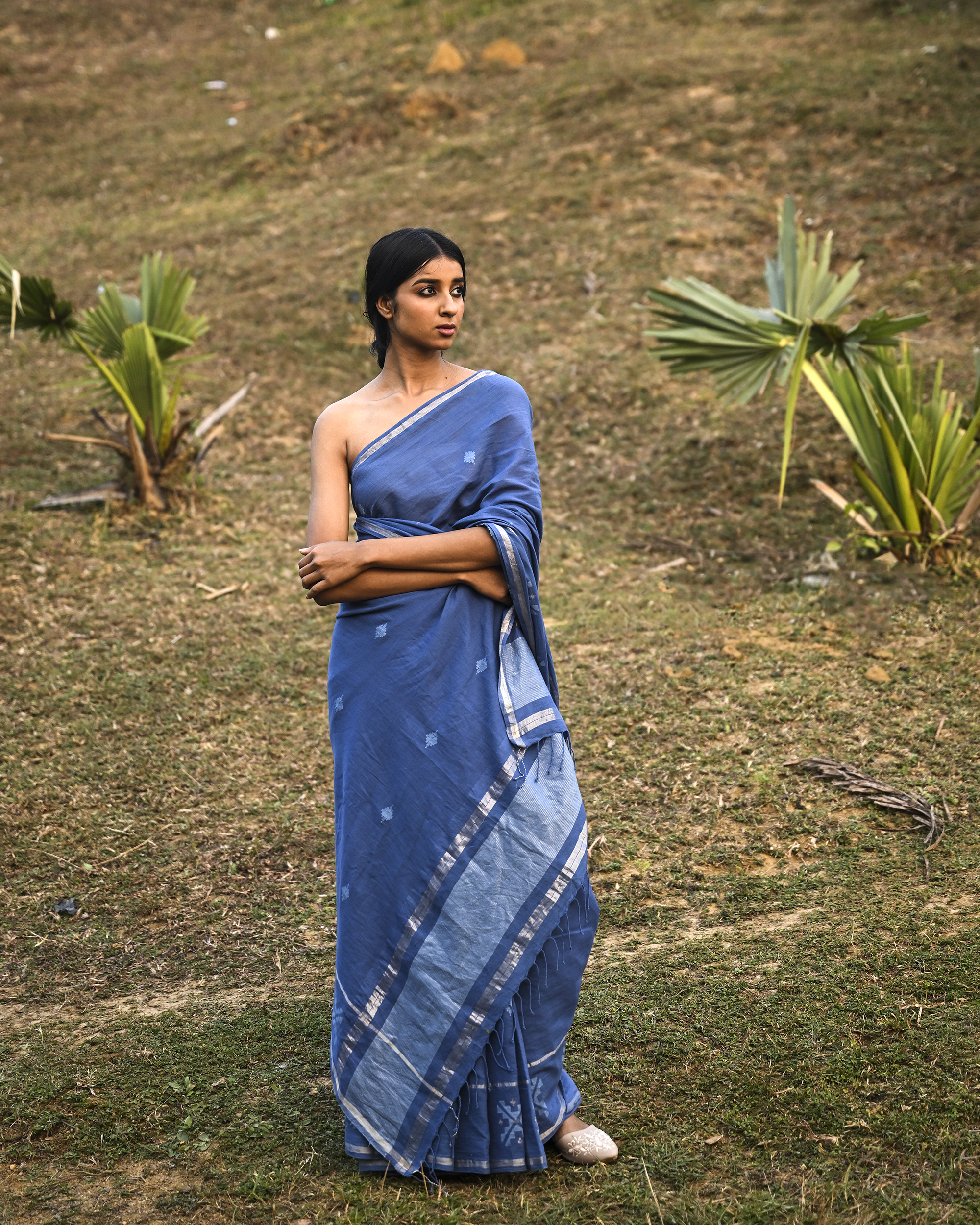 Model wearing the Dusty Blue Minimal Jamdani Saree, a handwoven dusty blue with a softly lustrous border Jamdani saree with sparse woven buttis with a minimal body and subtle pallu that mirrors the quiet elegance of the body.