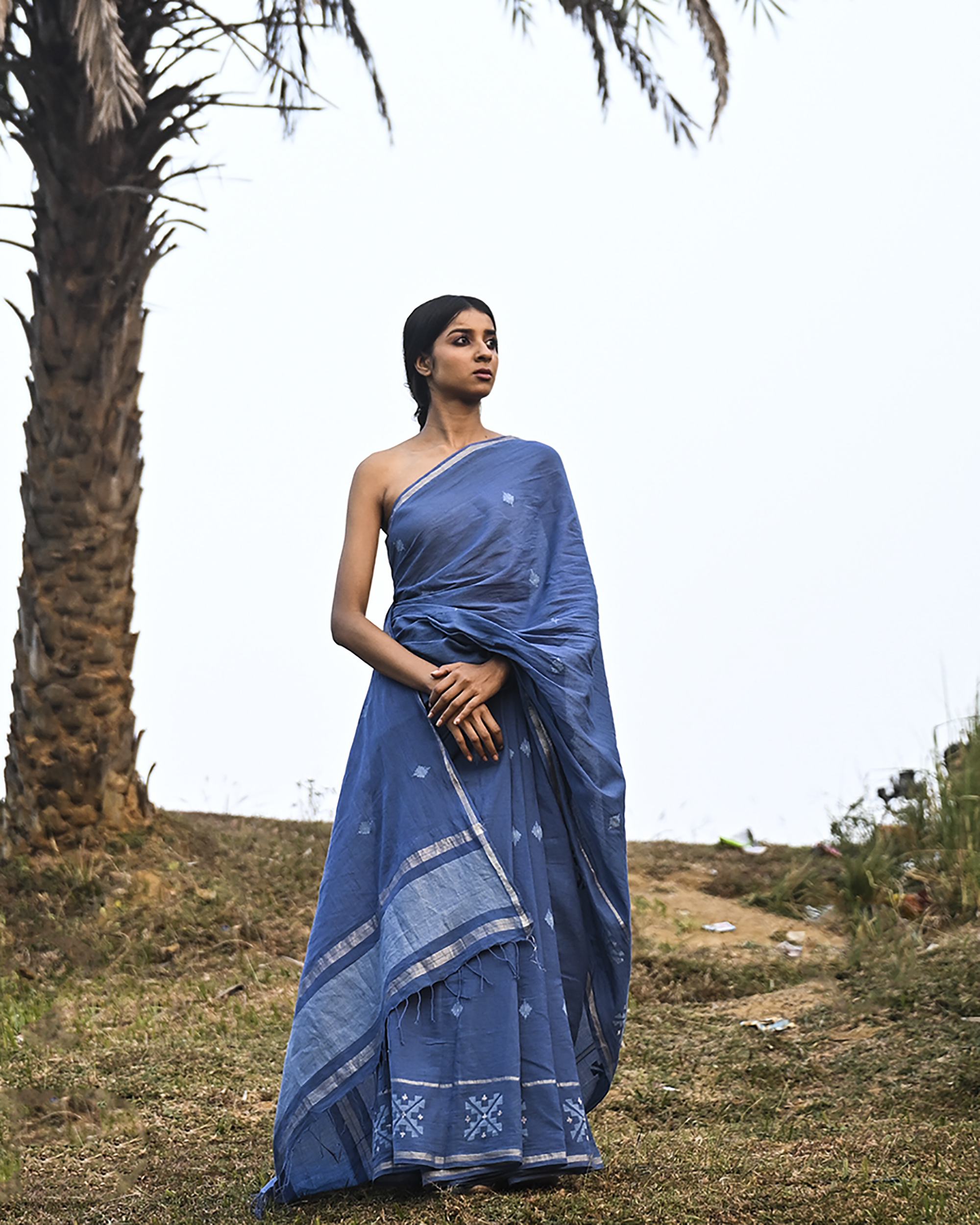 Model wearing the Dusty Blue Minimal Jamdani Saree, a handwoven dusty blue with a softly lustrous border Jamdani saree with sparse woven buttis with a minimal body and subtle pallu that mirrors the quiet elegance of the body.