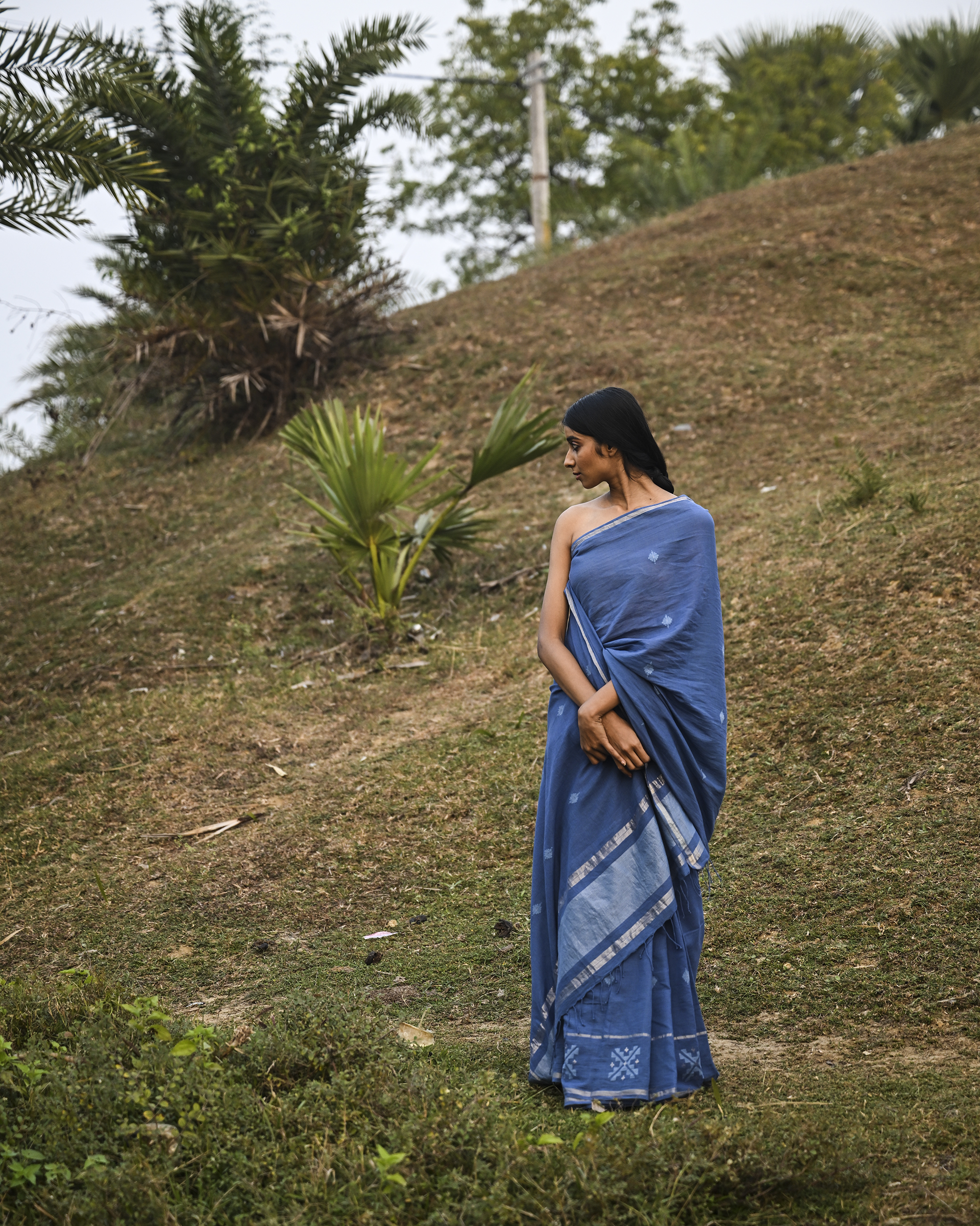 Model wearing the Dusty Blue Minimal Jamdani Saree, a handwoven dusty blue with a softly lustrous border Jamdani saree with sparse woven buttis with a minimal body and subtle pallu that mirrors the quiet elegance of the body.