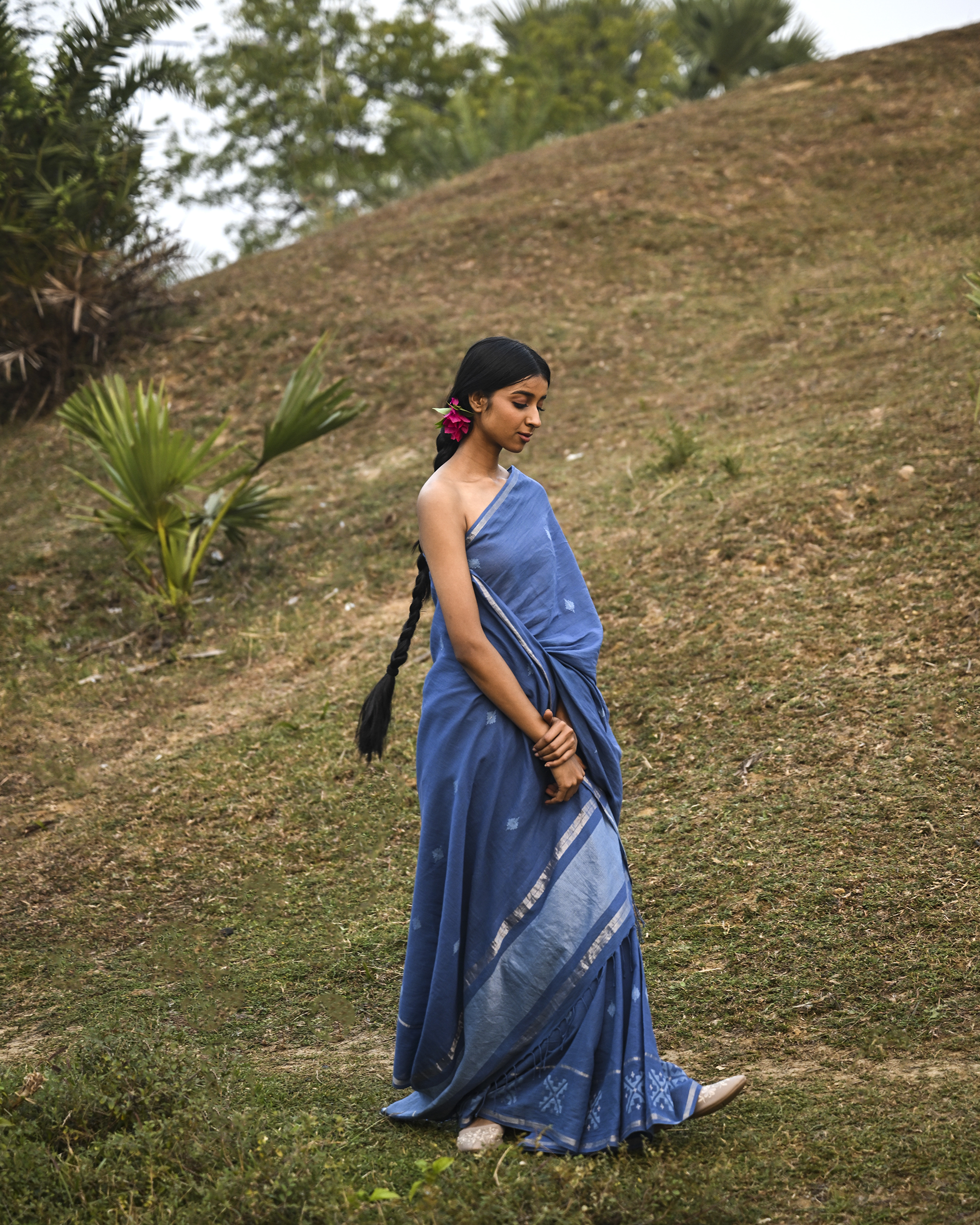 Model wearing the Dusty Blue Minimal Jamdani Saree, a handwoven dusty blue with a softly lustrous border Jamdani saree with sparse woven buttis with a minimal body and subtle pallu that mirrors the quiet elegance of the body.