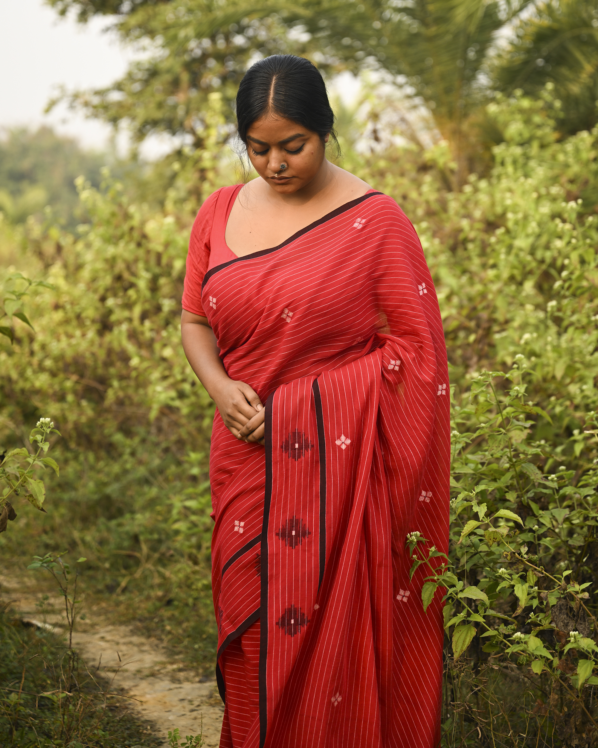 Model wearing the Vermilion Linear Jamdani Saree, a handwoven vermilion red with black-edged borders Jamdani saree with fine linear rhythm with scattered woven motifs and graphic pallu with sharp contrast-led edging.