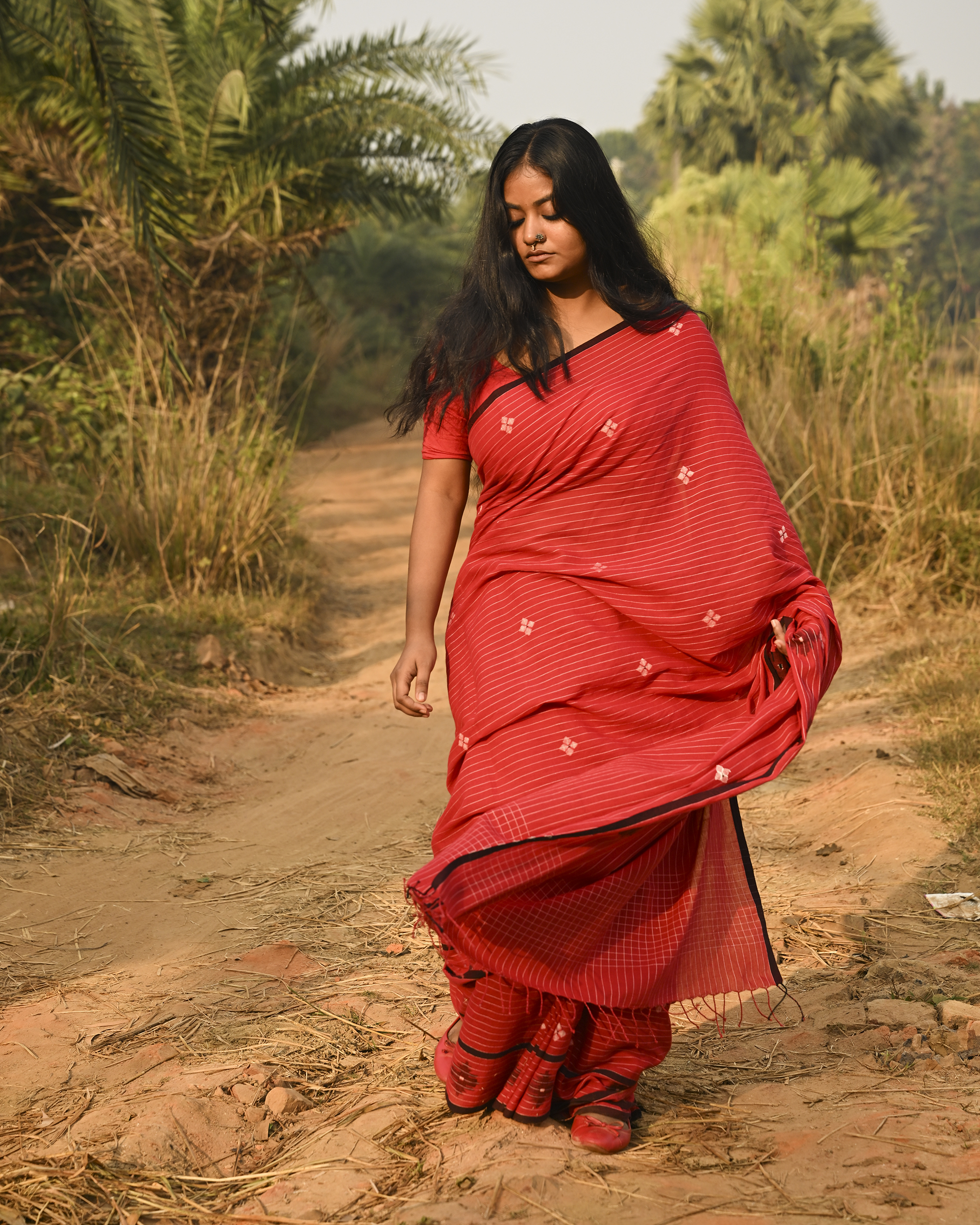 Model wearing the Vermilion Linear Jamdani Saree, a handwoven vermilion red with black-edged borders Jamdani saree with fine linear rhythm with scattered woven motifs and graphic pallu with sharp contrast-led edging.
