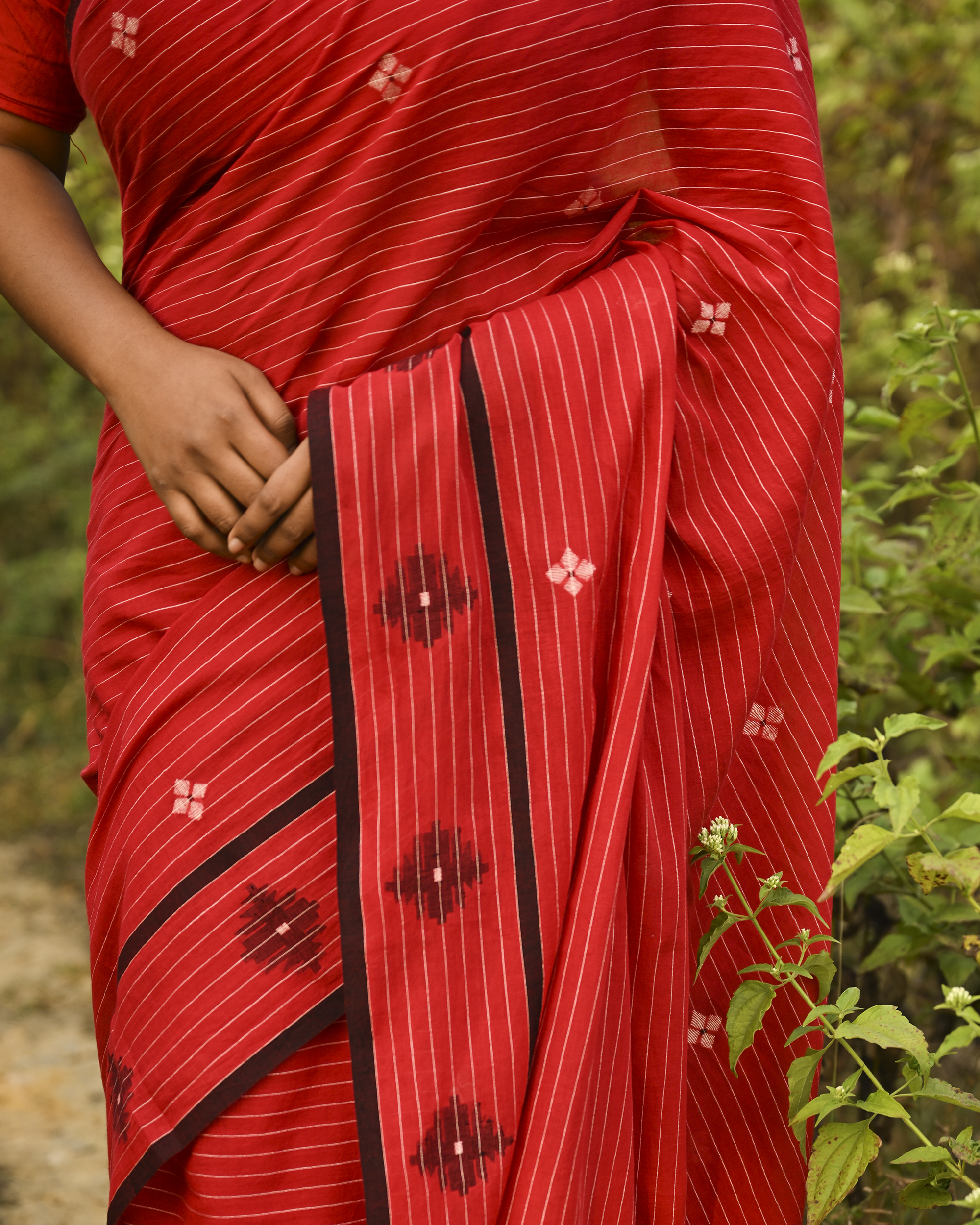 Model wearing the Vermilion Linear Jamdani Saree, a handwoven vermilion red with black-edged borders Jamdani saree with fine linear rhythm with scattered woven motifs and graphic pallu with sharp contrast-led edging.