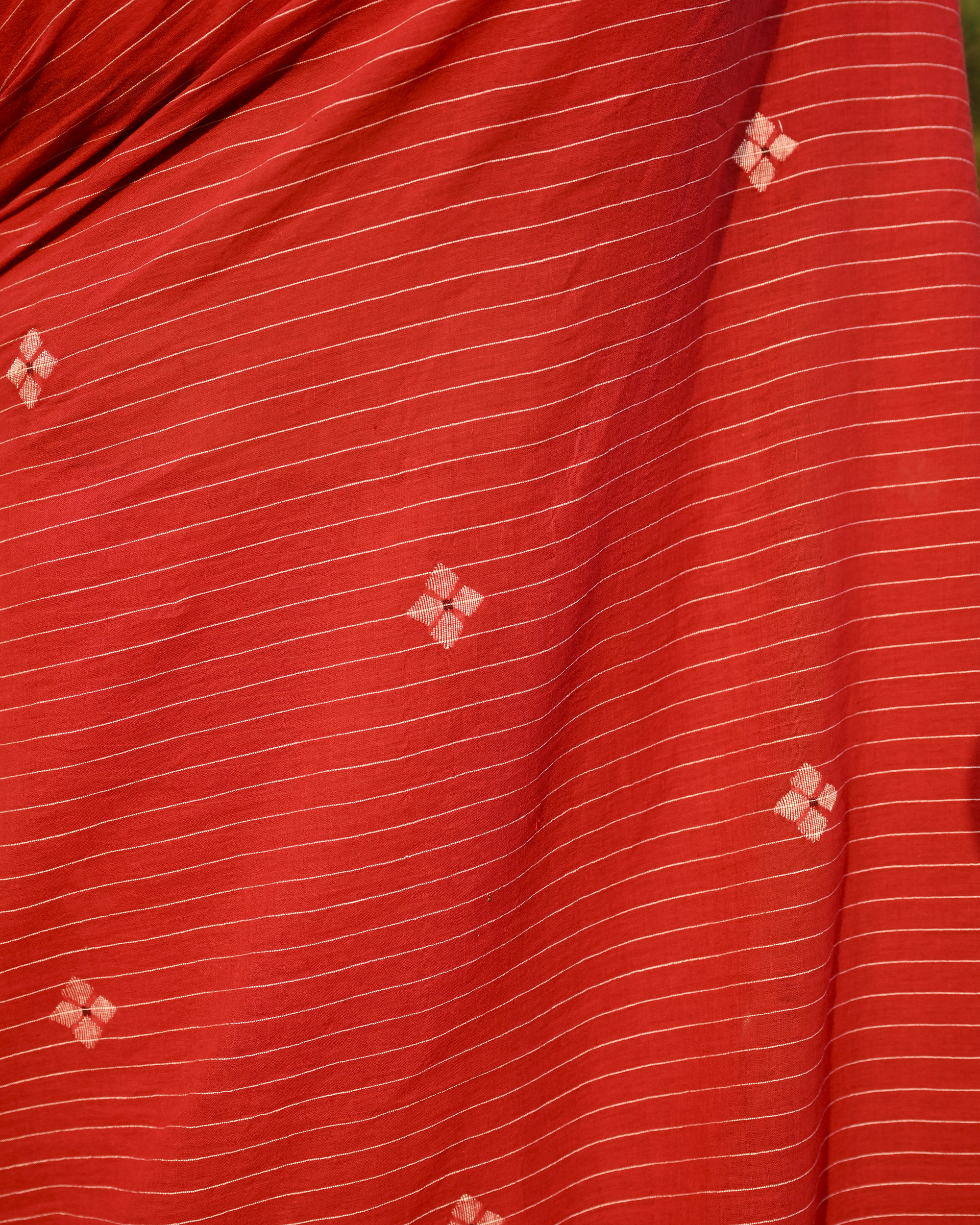 Model wearing the Vermilion Linear Jamdani Saree, a handwoven vermilion red with black-edged borders Jamdani saree with fine linear rhythm with scattered woven motifs and graphic pallu with sharp contrast-led edging.