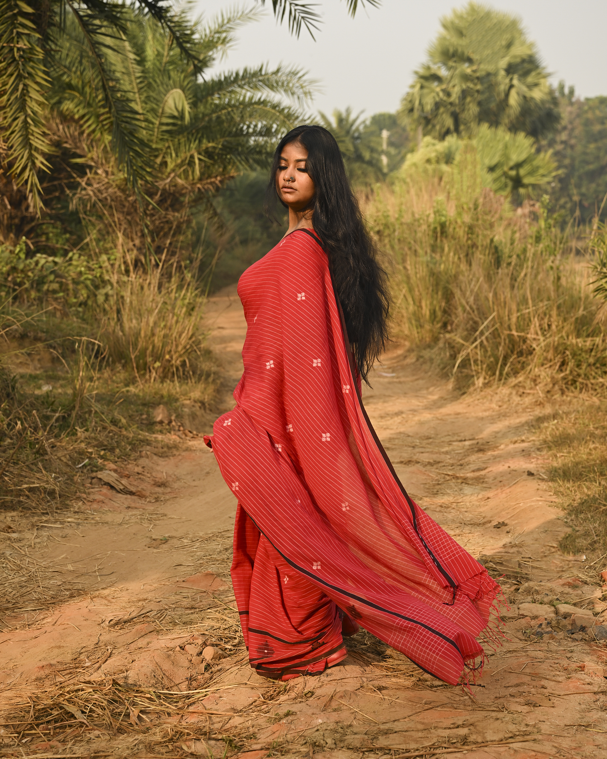Model wearing the Vermilion Linear Jamdani Saree, a handwoven vermilion red with black-edged borders Jamdani saree with fine linear rhythm with scattered woven motifs and graphic pallu with sharp contrast-led edging.