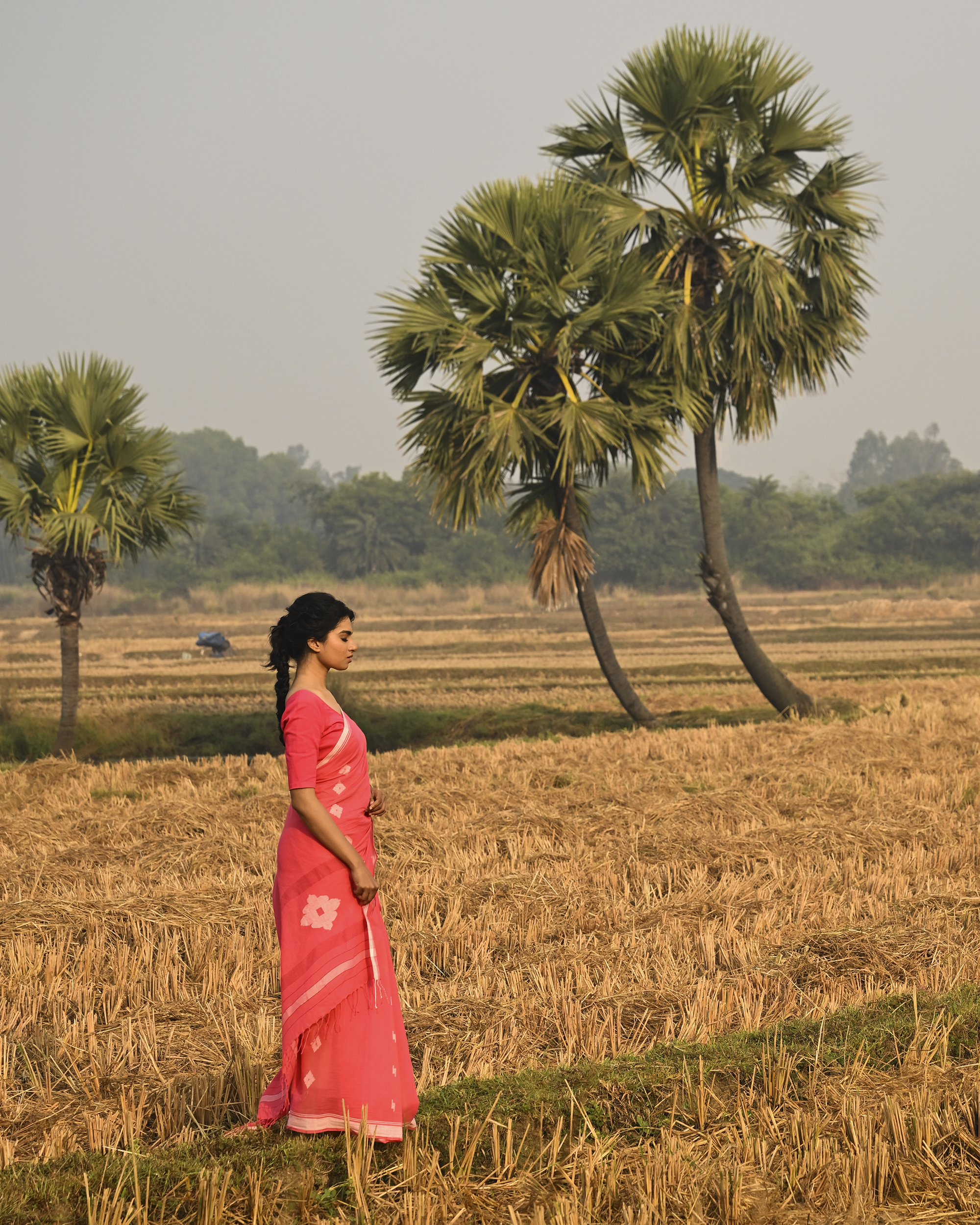 Model wearing the Coral Buti Jamdani Saree, a handwoven fresh coral-pink with white motifs Jamdani saree with tiny white butis scattered across the body and softly open pallu with delicate woven detail.