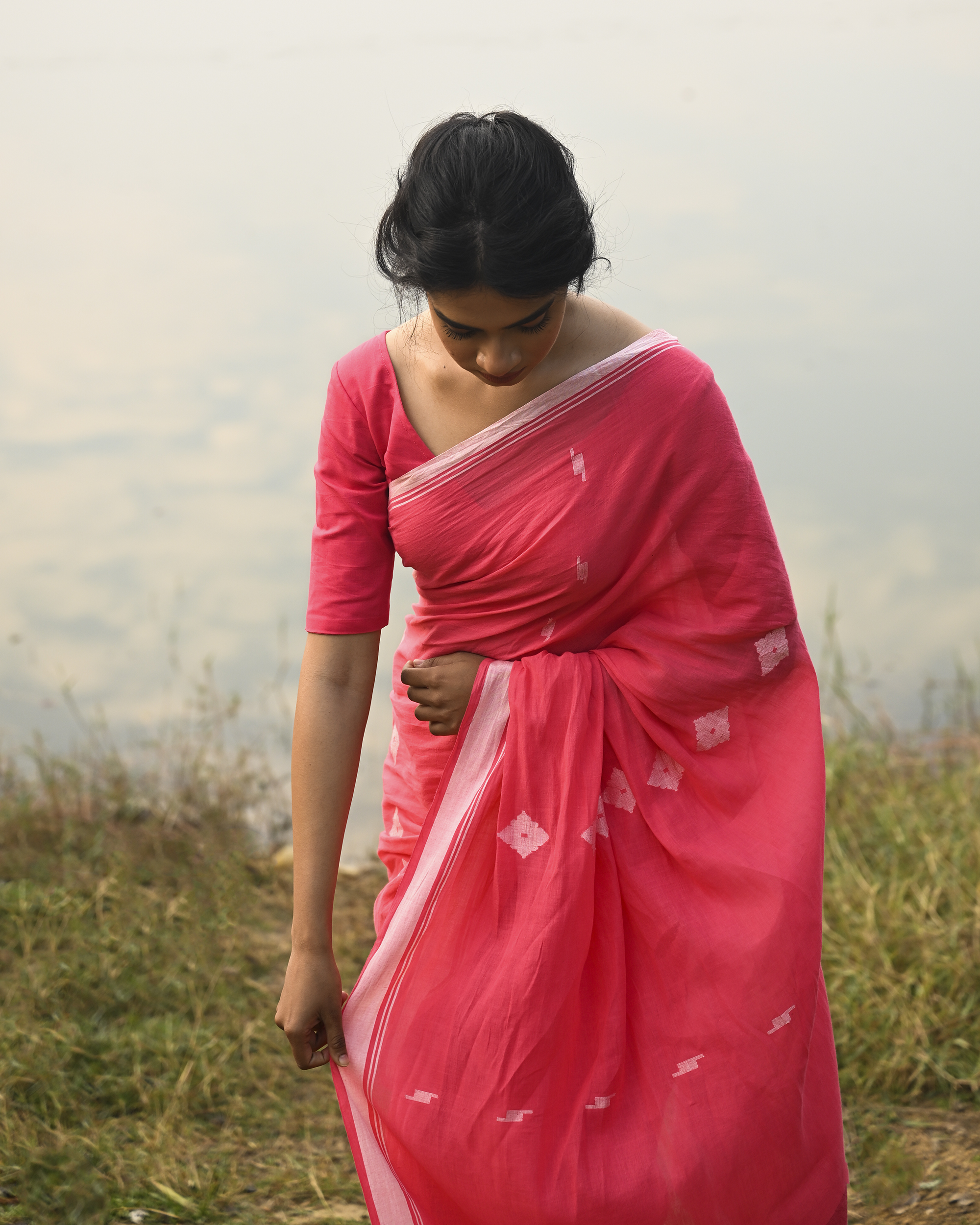 Model wearing the Coral Buti Jamdani Saree, a handwoven fresh coral-pink with white motifs Jamdani saree with tiny white butis scattered across the body and softly open pallu with delicate woven detail.