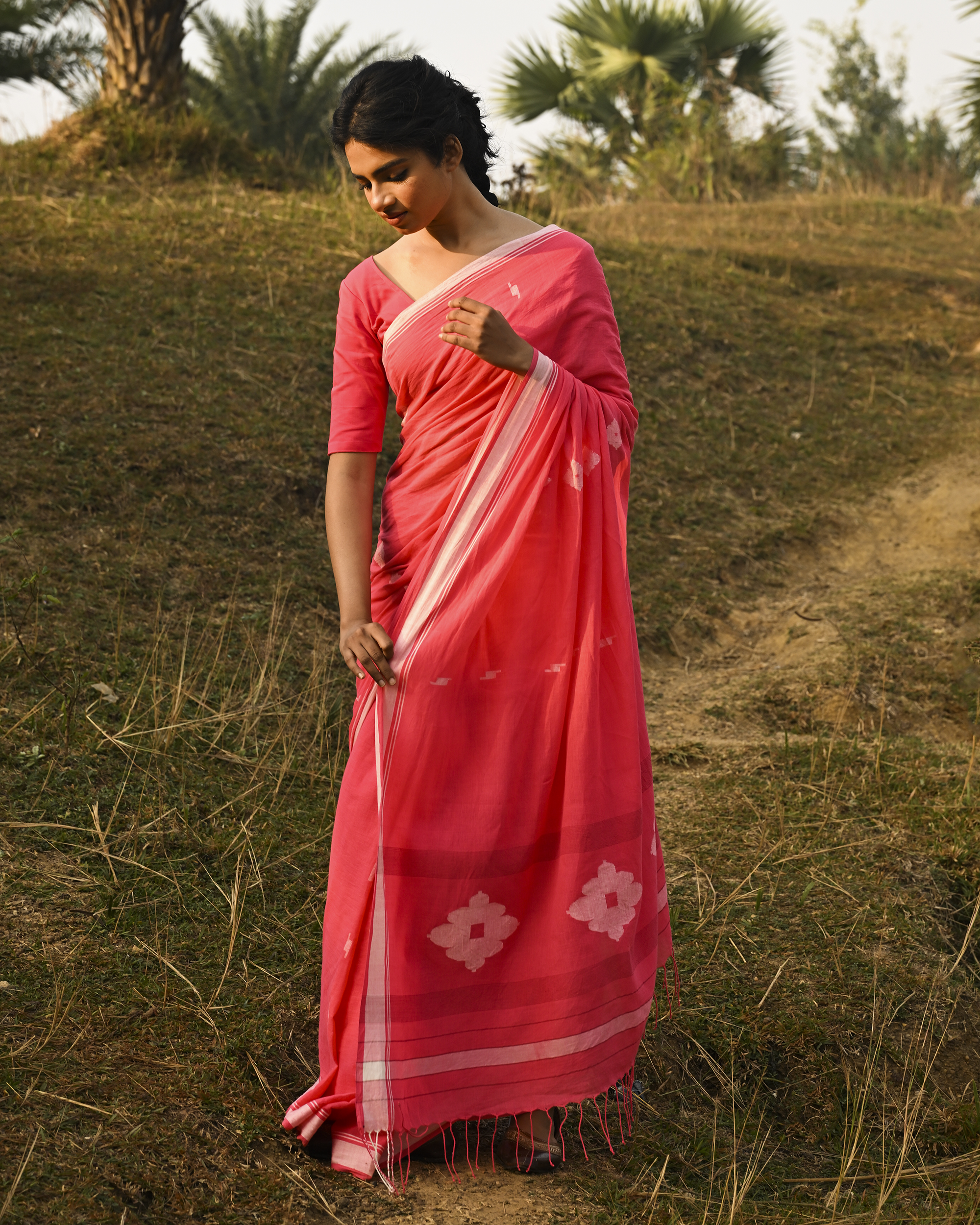 Model wearing the Coral Buti Jamdani Saree, a handwoven fresh coral-pink with white motifs Jamdani saree with tiny white butis scattered across the body and softly open pallu with delicate woven detail.
