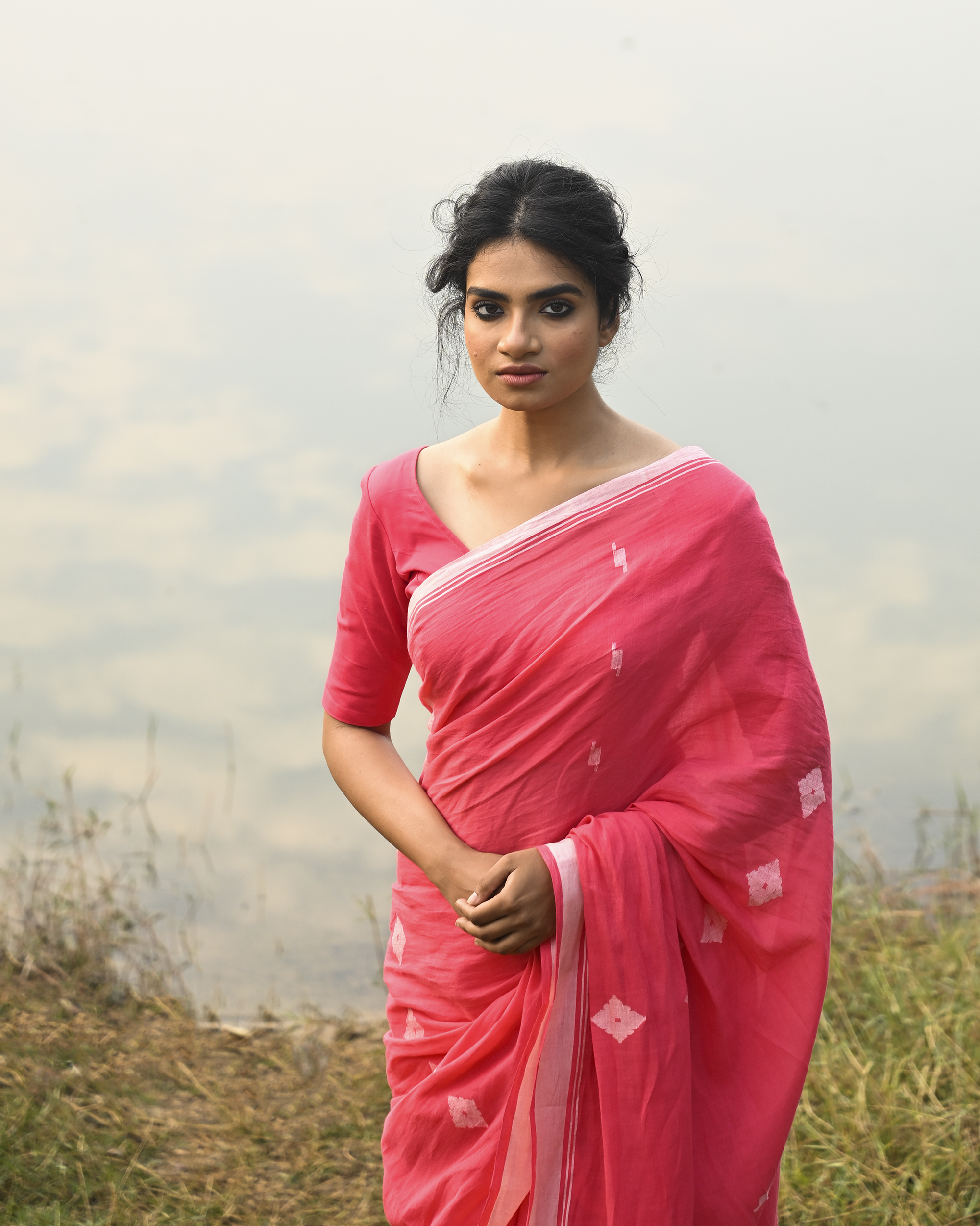 Model wearing the Coral Buti Jamdani Saree, a handwoven fresh coral-pink with white motifs Jamdani saree with tiny white butis scattered across the body and softly open pallu with delicate woven detail.