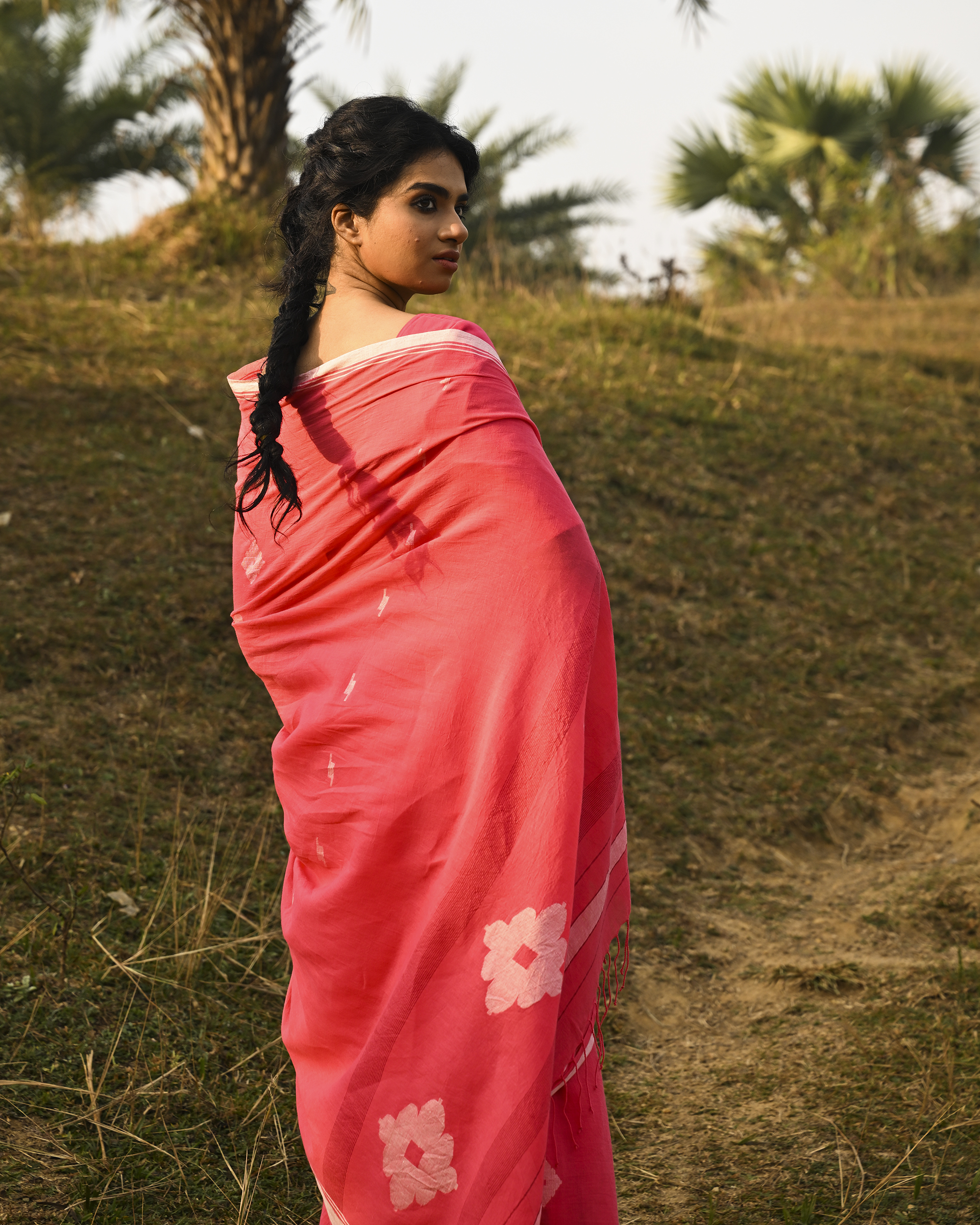 Model wearing the Coral Buti Jamdani Saree, a handwoven fresh coral-pink with white motifs Jamdani saree with tiny white butis scattered across the body and softly open pallu with delicate woven detail.