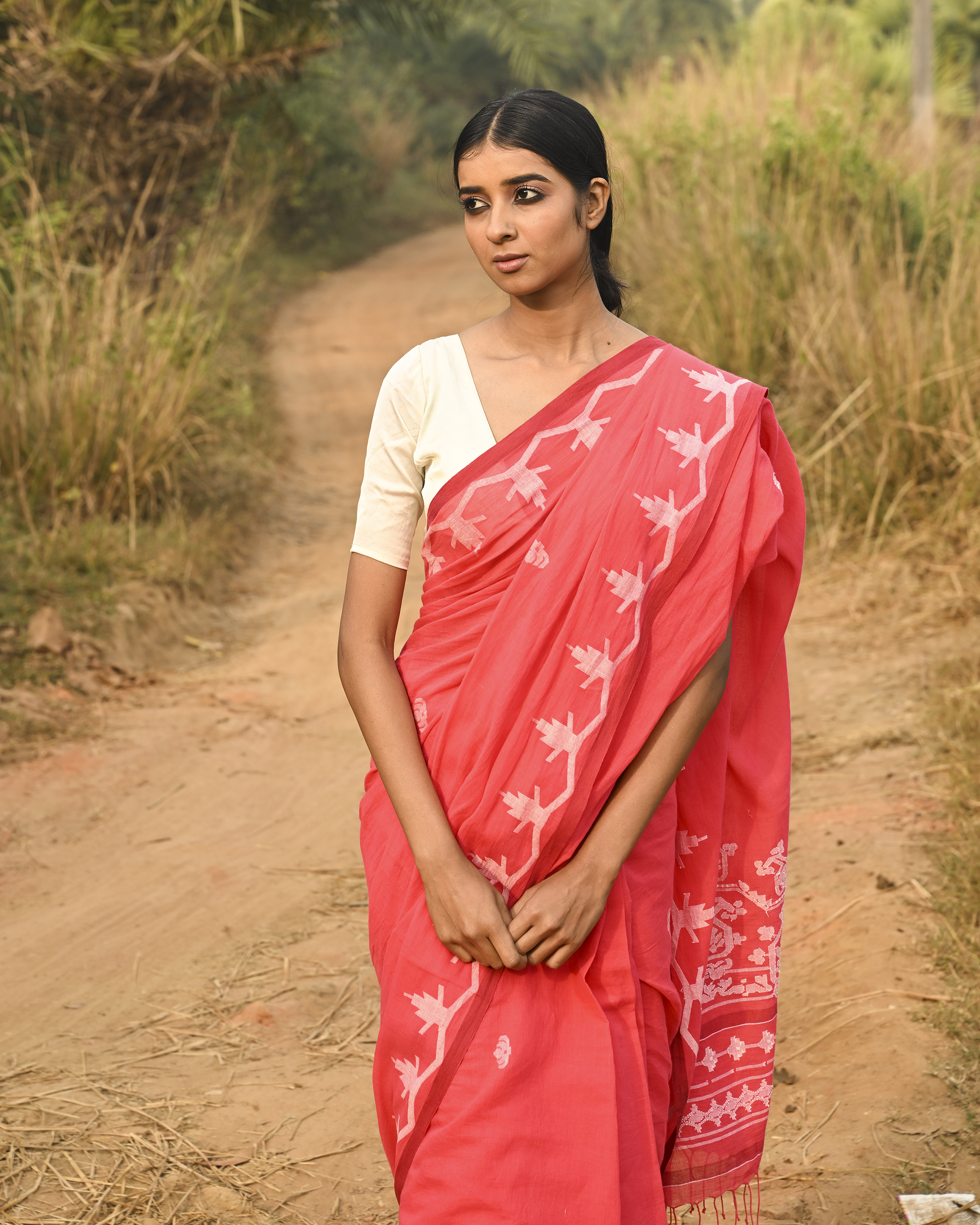 Model wearing the Coral Vine-Border Jamdani Saree, a handwoven bright coral with white woven details Jamdani saree with delicate body motifs with a lyrical vine-like border and border-forward pallu with movement and visual rhythm.