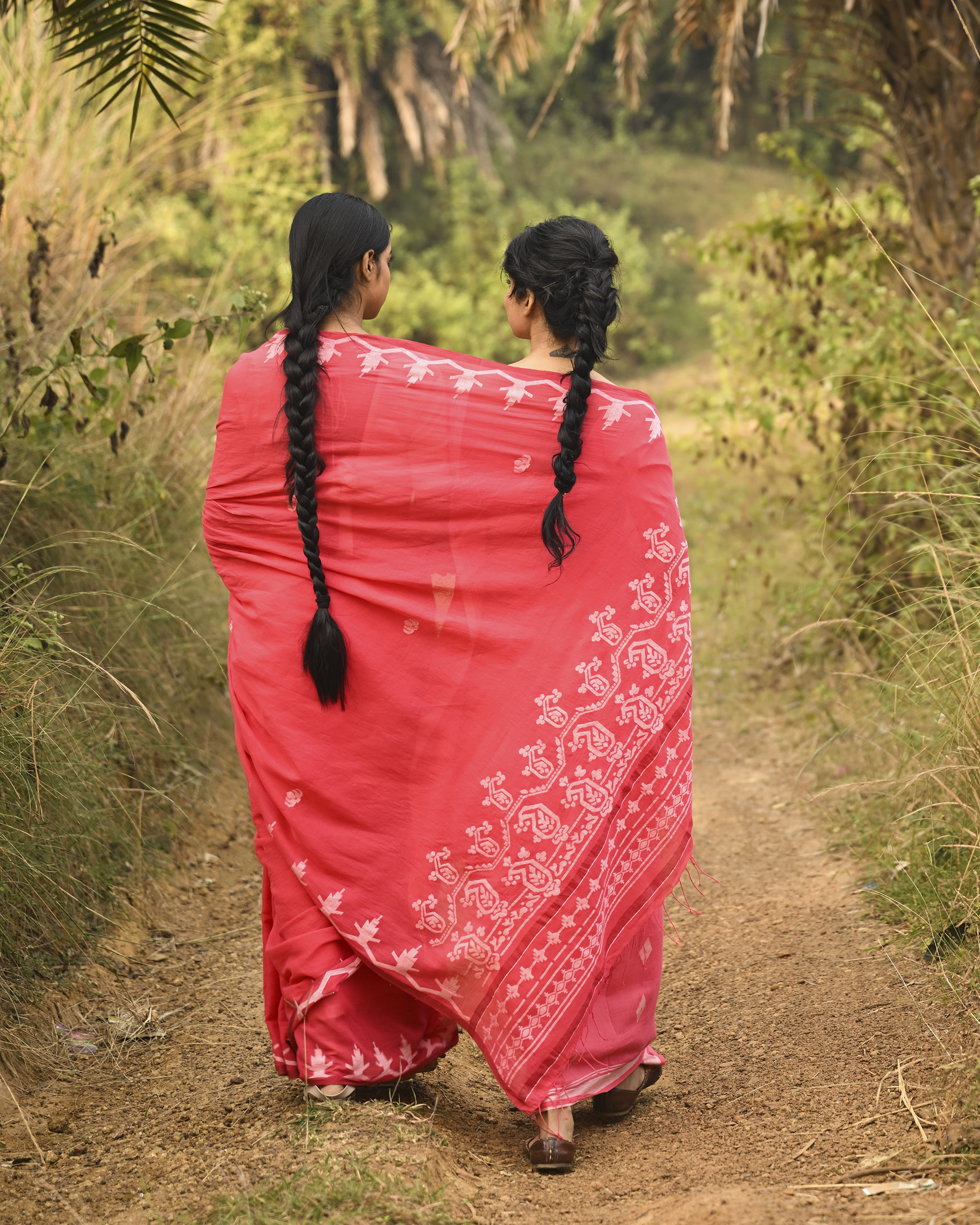 Model wearing the Coral Vine-Border Jamdani Saree, a handwoven bright coral with white woven details Jamdani saree with delicate body motifs with a lyrical vine-like border and border-forward pallu with movement and visual rhythm.