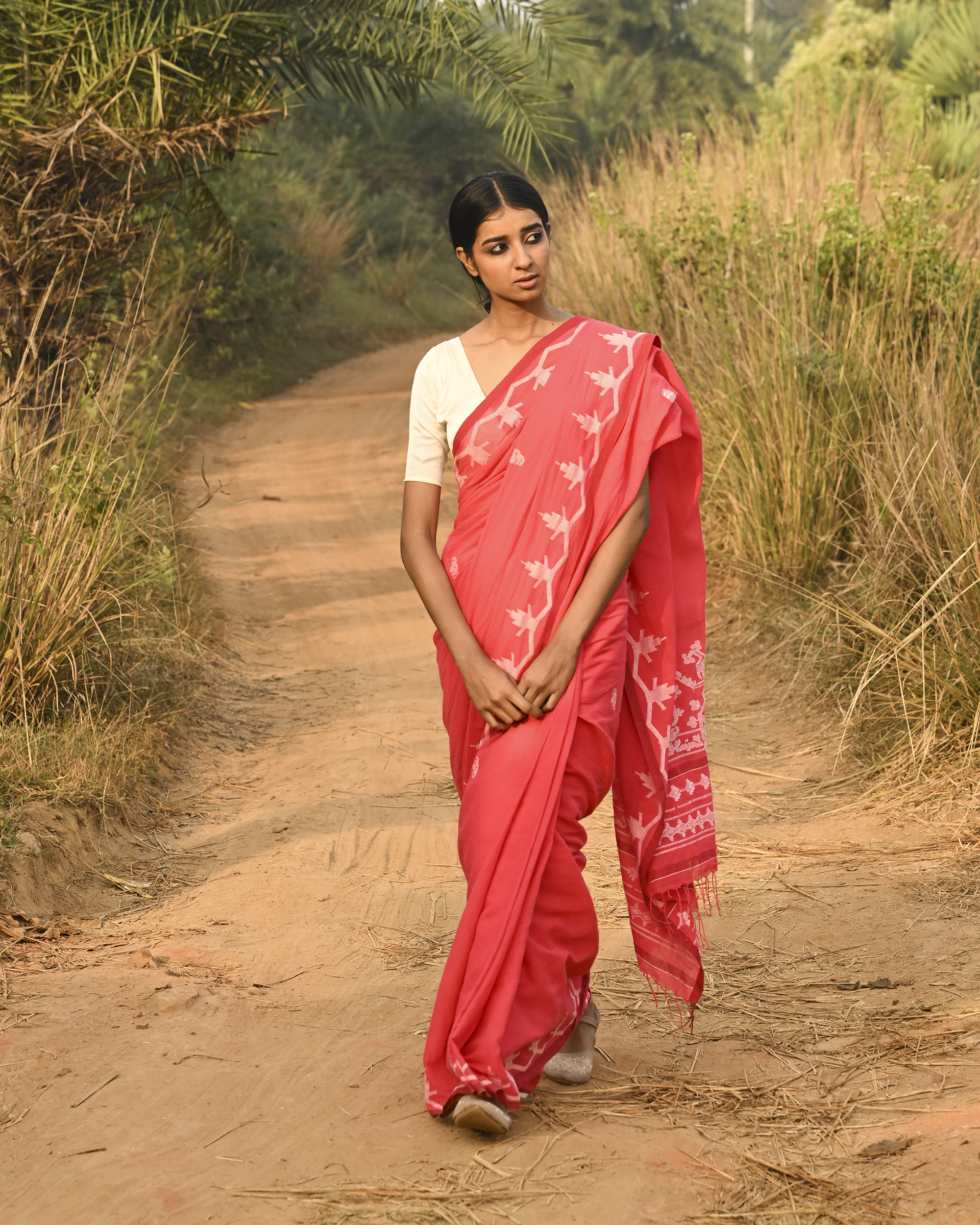 Model wearing the Coral Vine-Border Jamdani Saree, a handwoven bright coral with white woven details Jamdani saree with delicate body motifs with a lyrical vine-like border and border-forward pallu with movement and visual rhythm.