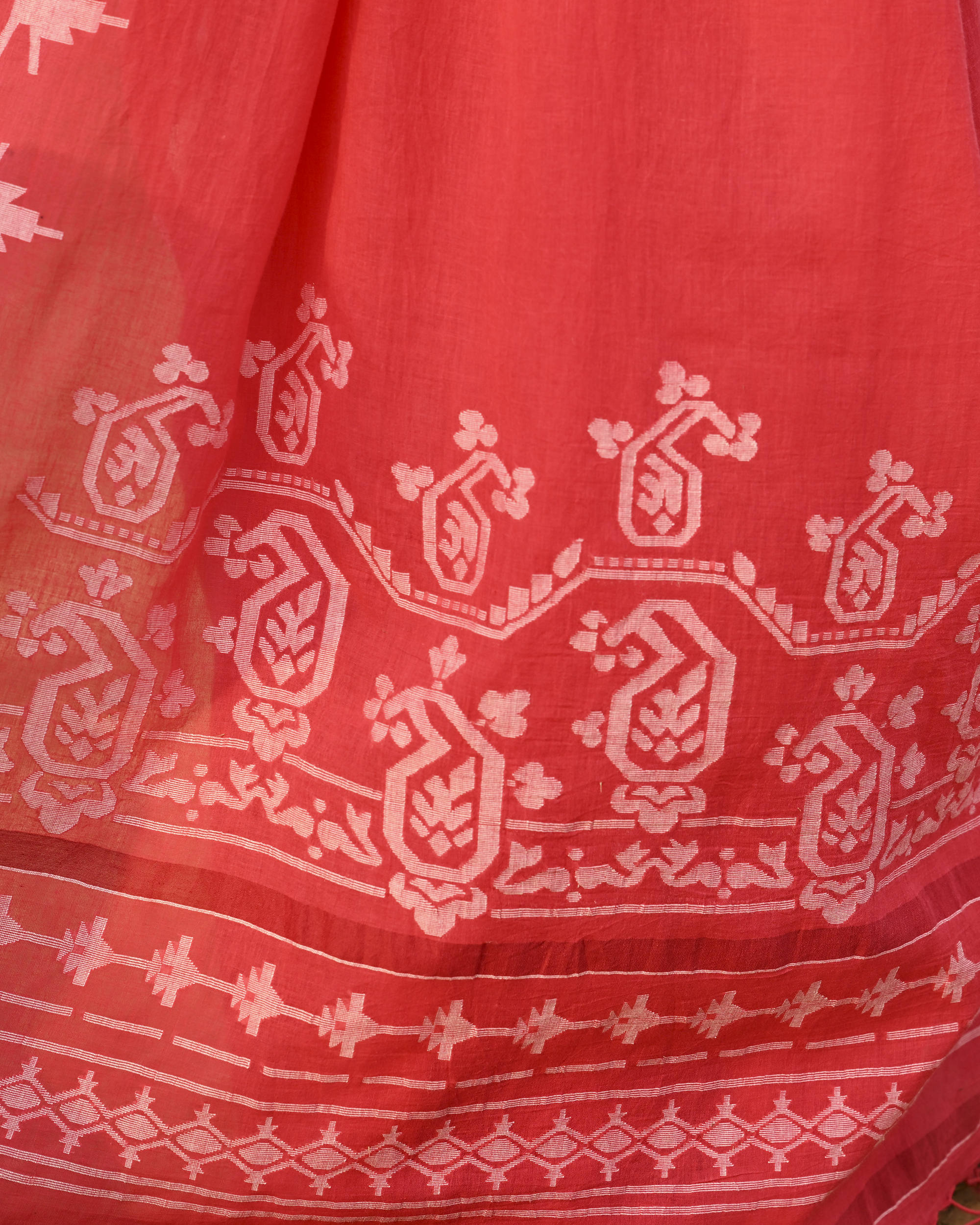 Model wearing the Coral Vine-Border Jamdani Saree, a handwoven bright coral with white woven details Jamdani saree with delicate body motifs with a lyrical vine-like border and border-forward pallu with movement and visual rhythm.