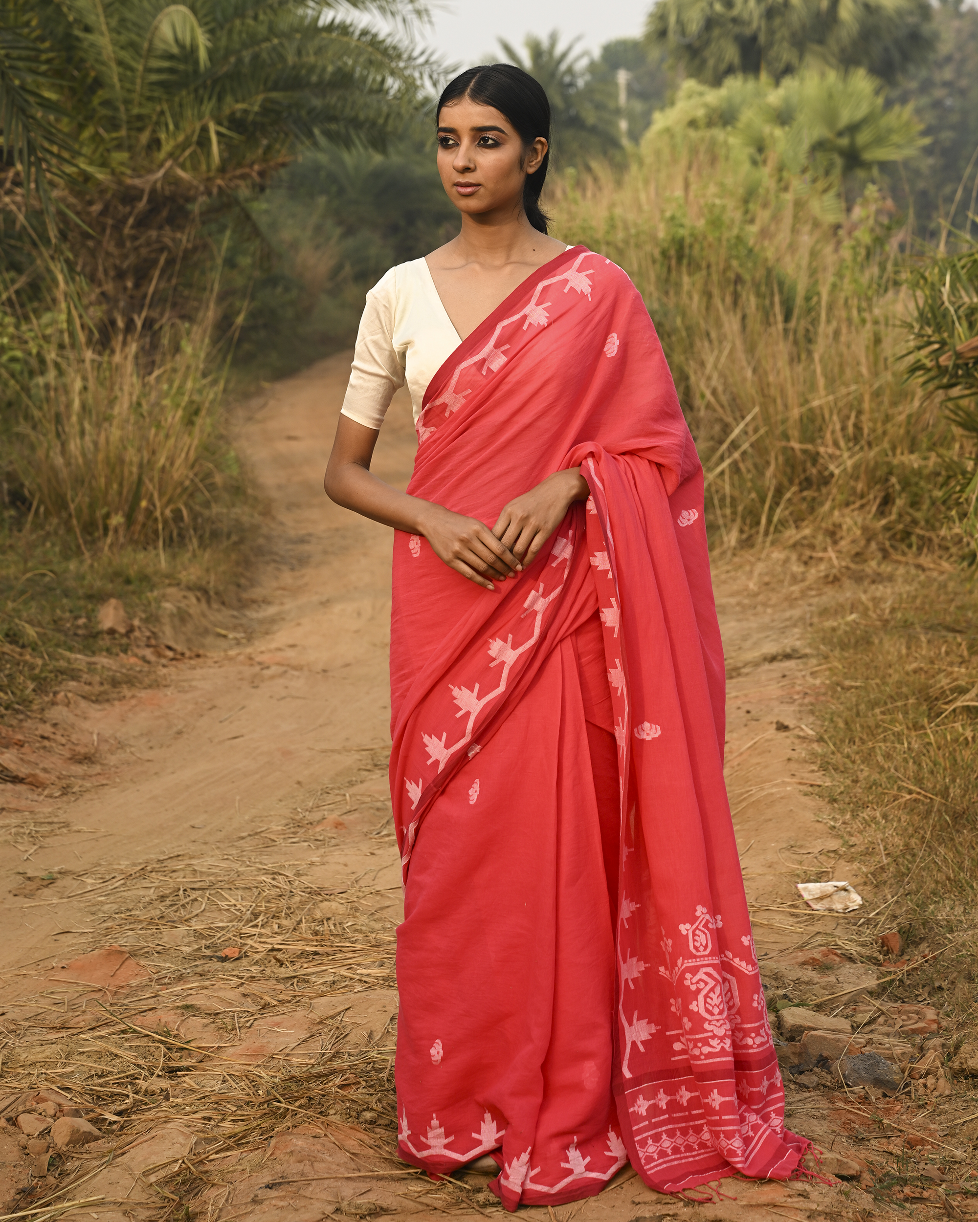 Model wearing the Coral Vine-Border Jamdani Saree, a handwoven bright coral with white woven details Jamdani saree with delicate body motifs with a lyrical vine-like border and border-forward pallu with movement and visual rhythm.
