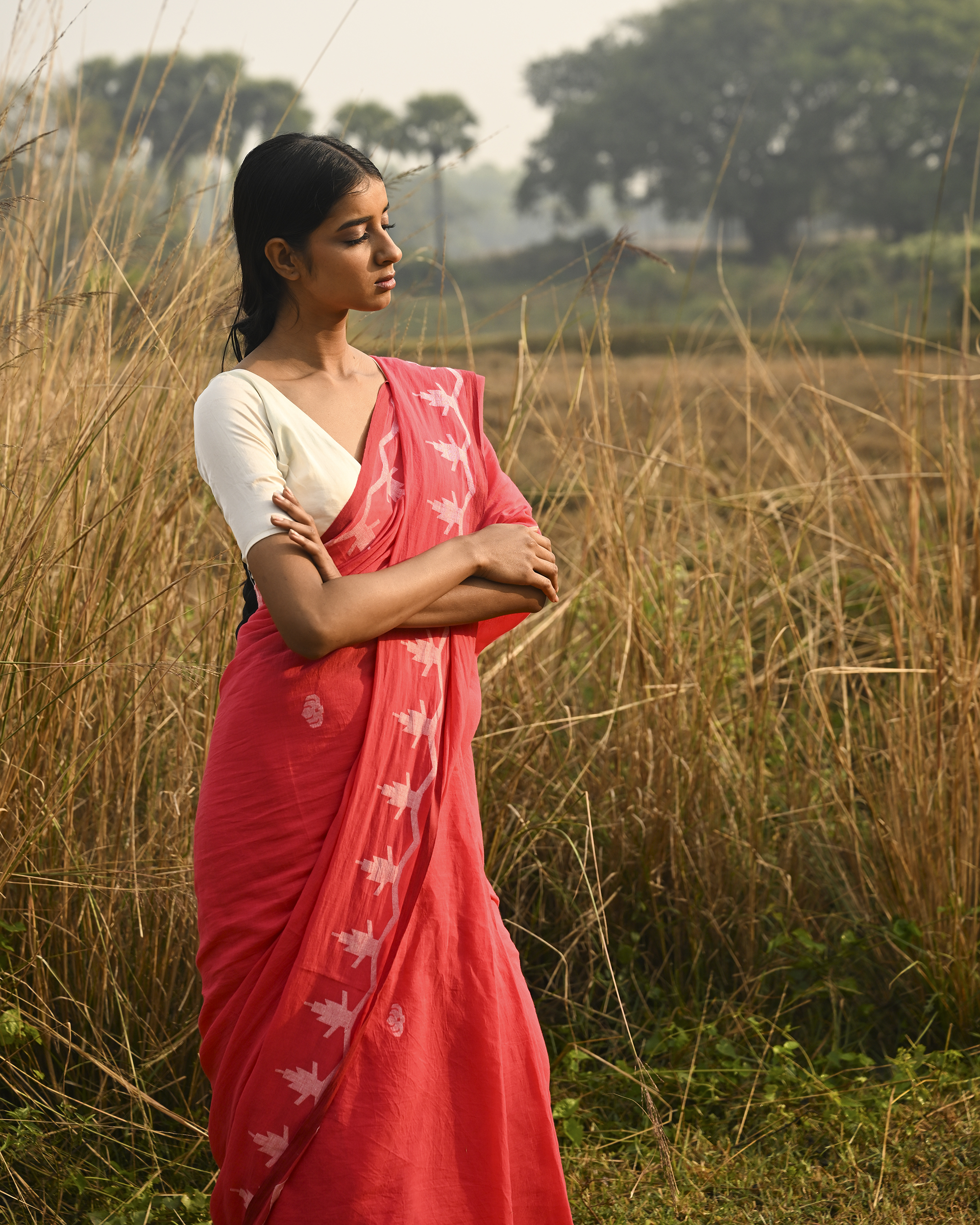 Model wearing the Coral Vine-Border Jamdani Saree, a handwoven bright coral with white woven details Jamdani saree with delicate body motifs with a lyrical vine-like border and border-forward pallu with movement and visual rhythm.