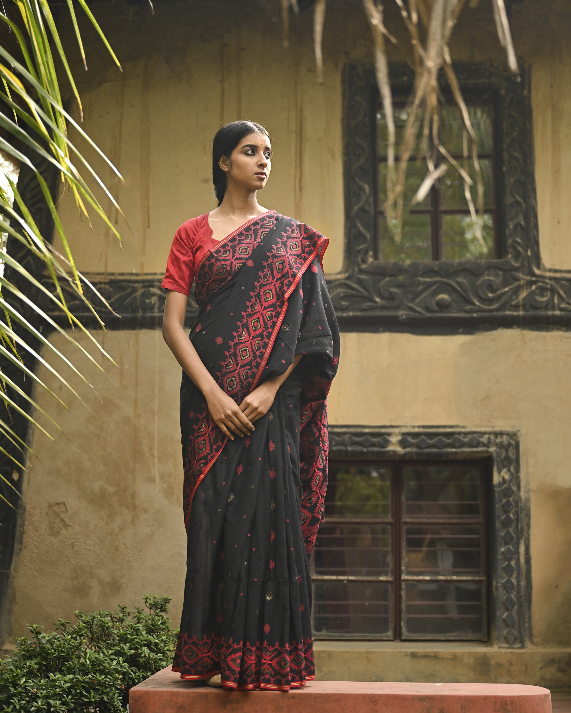 Model wearing the Black Crimson Jamdani Saree, a handwoven black with deep red woven geometry Jamdani saree with scattered motifs with bold red geometric work and dramatic pallu with deep contrast and strong patterning.