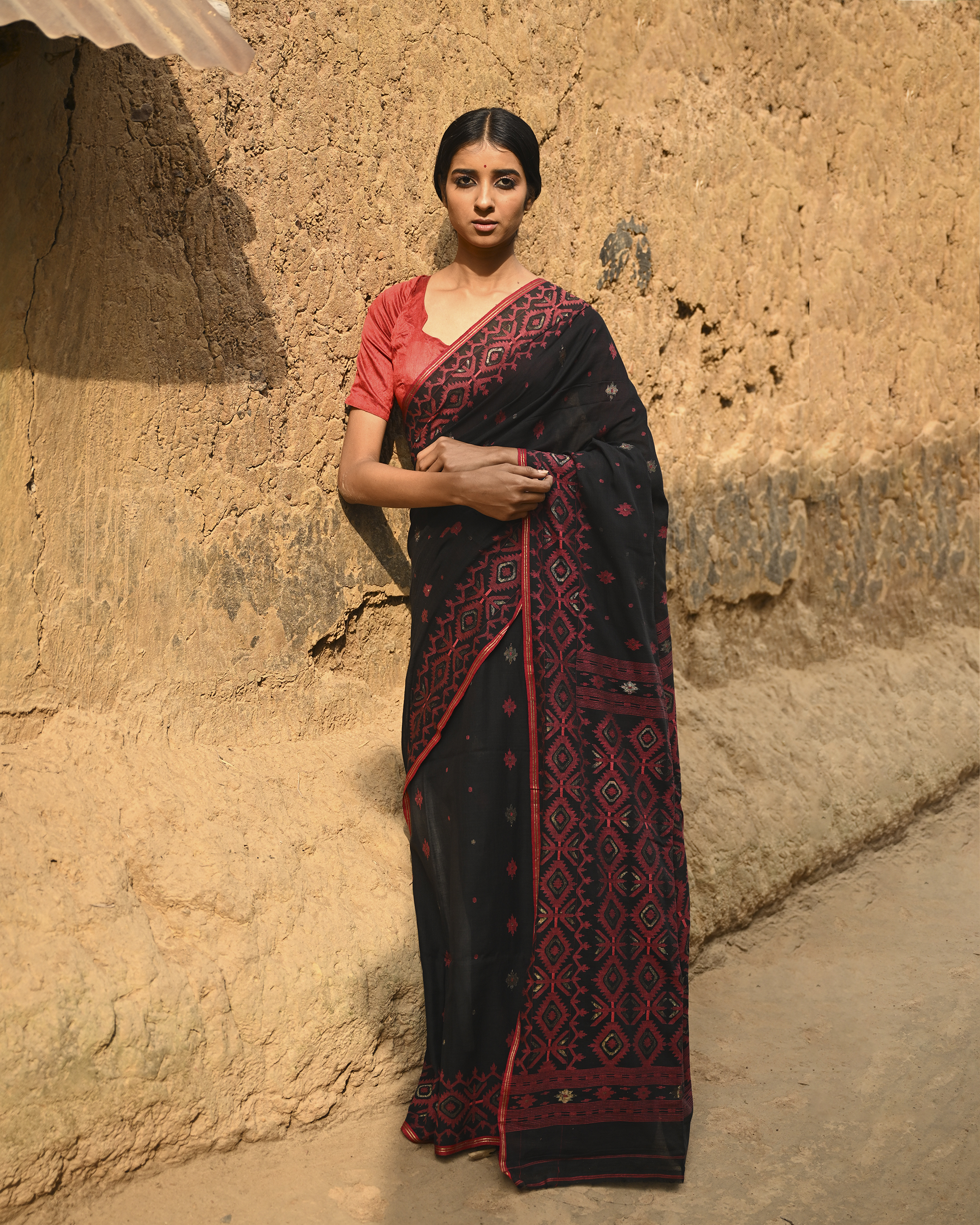 Model wearing the Black Crimson Jamdani Saree, a handwoven black with deep red woven geometry Jamdani saree with scattered motifs with bold red geometric work and dramatic pallu with deep contrast and strong patterning.