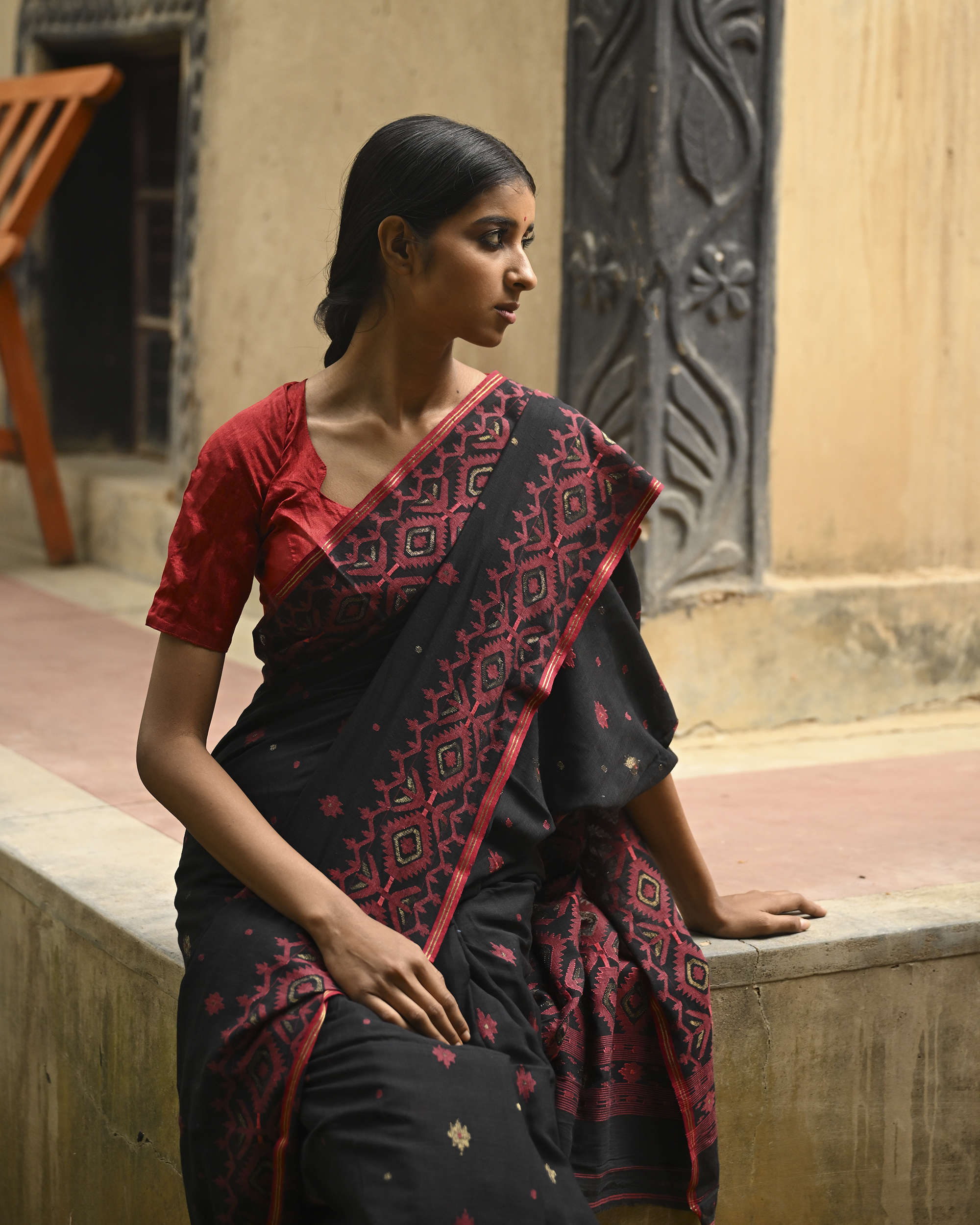 Model wearing the Black Crimson Jamdani Saree, a handwoven black with deep red woven geometry Jamdani saree with scattered motifs with bold red geometric work and dramatic pallu with deep contrast and strong patterning.