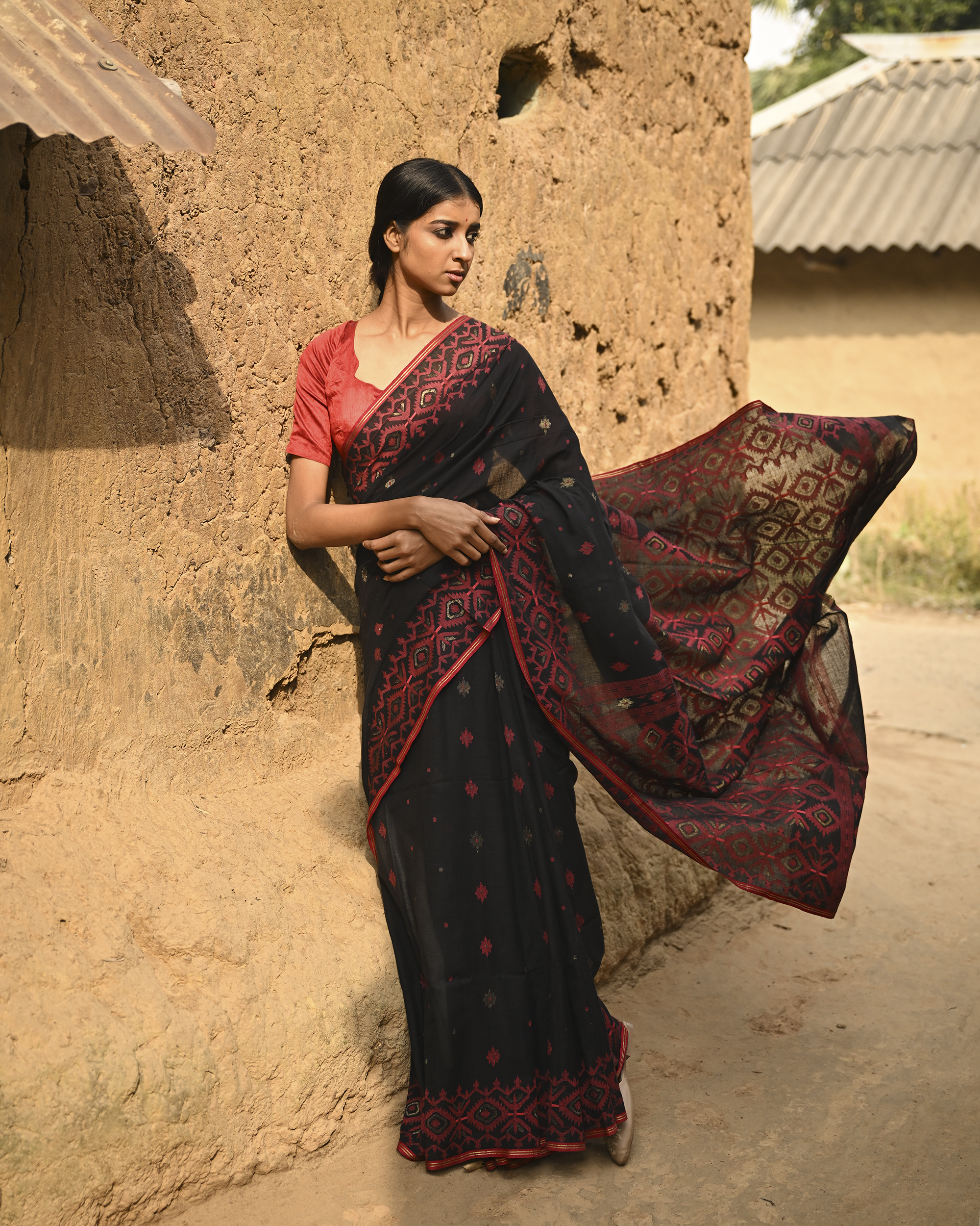 Model wearing the Black Crimson Jamdani Saree, a handwoven black with deep red woven geometry Jamdani saree with scattered motifs with bold red geometric work and dramatic pallu with deep contrast and strong patterning.
