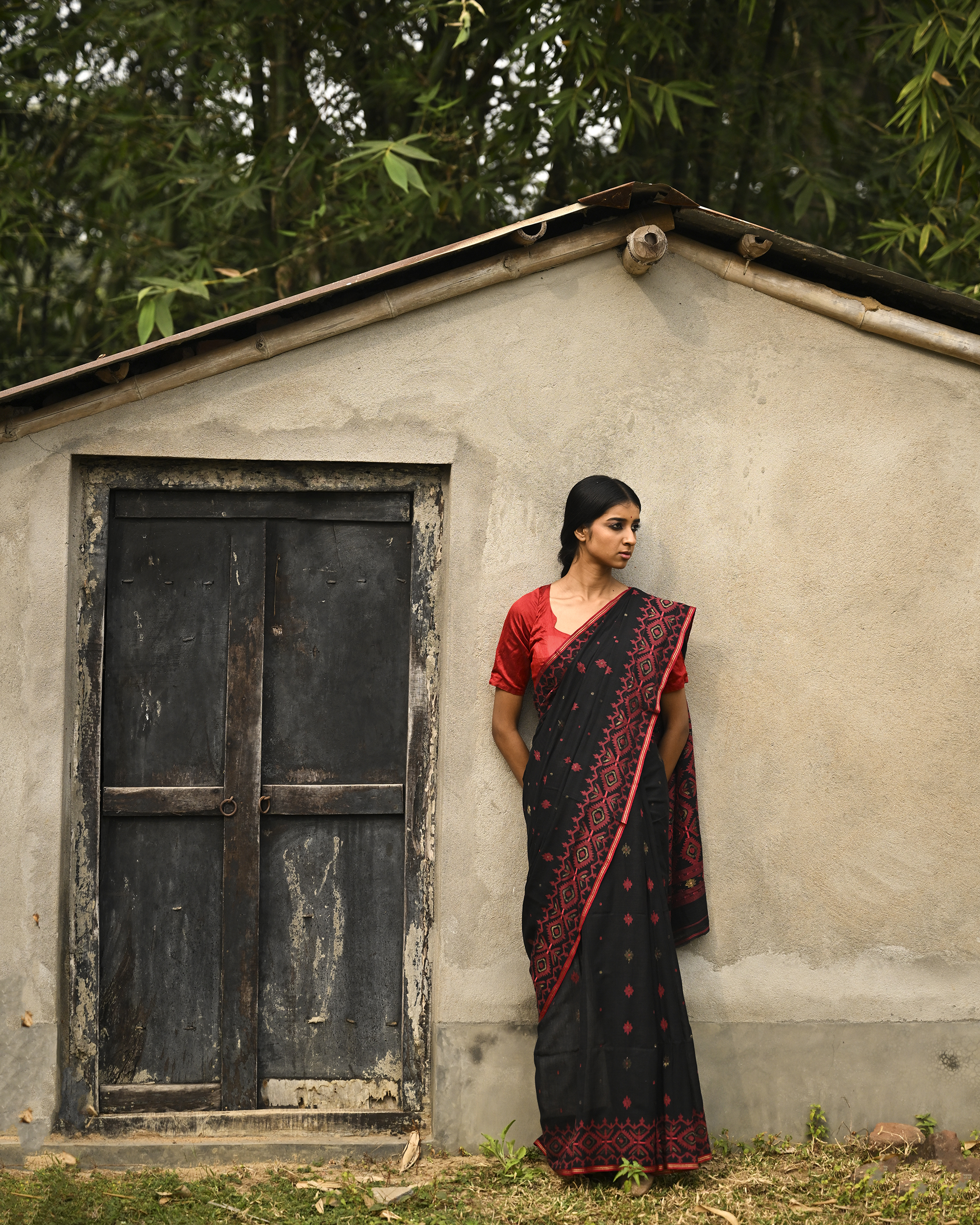 Model wearing the Black Crimson Jamdani Saree, a handwoven black with deep red woven geometry Jamdani saree with scattered motifs with bold red geometric work and dramatic pallu with deep contrast and strong patterning.