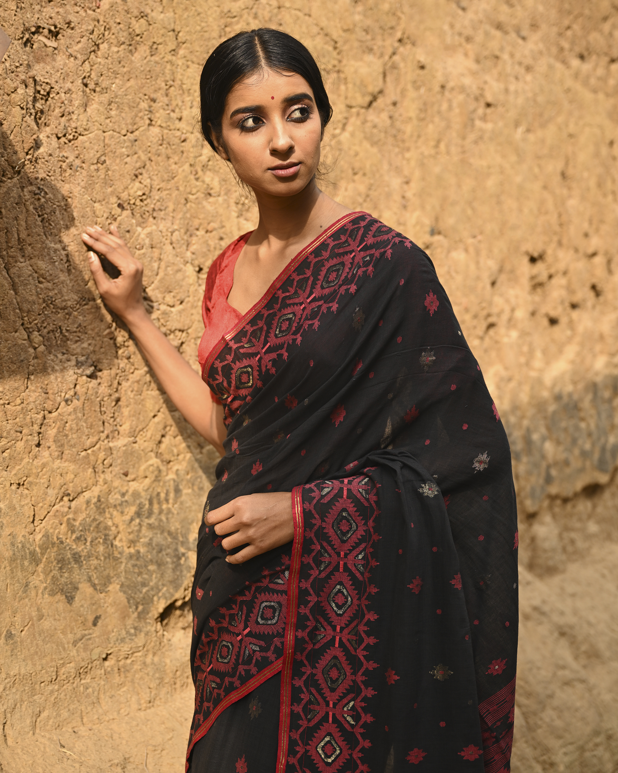 Model wearing the Black Crimson Jamdani Saree, a handwoven black with deep red woven geometry Jamdani saree with scattered motifs with bold red geometric work and dramatic pallu with deep contrast and strong patterning.