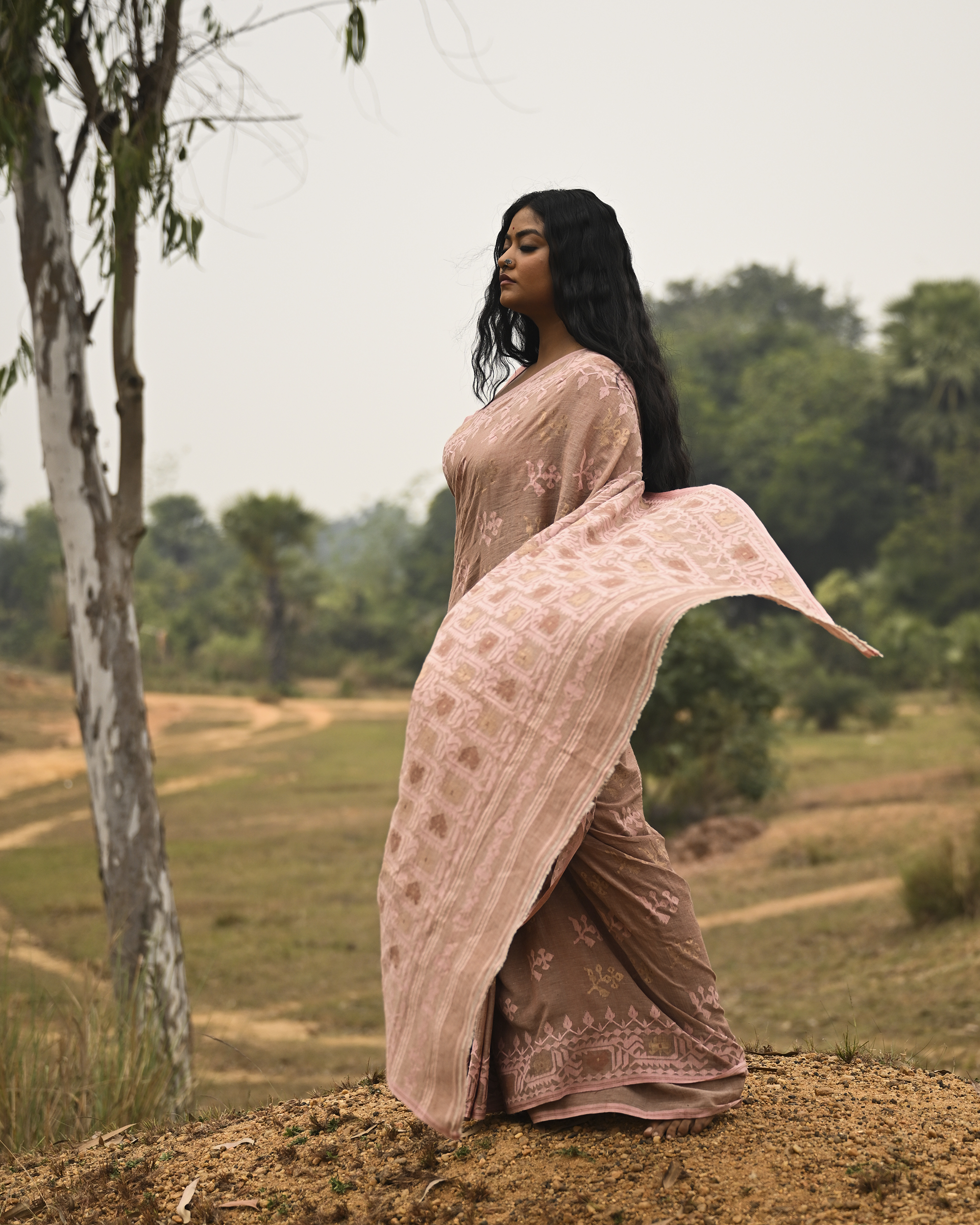 Model wearing the Blush Nude Pastel Jamdani Saree, a handwoven blush nude with pastel rose and muted gold weave Jamdani saree with rich woven body and border work with soft pastel accents and heavily detailed pallu made to be worn open.