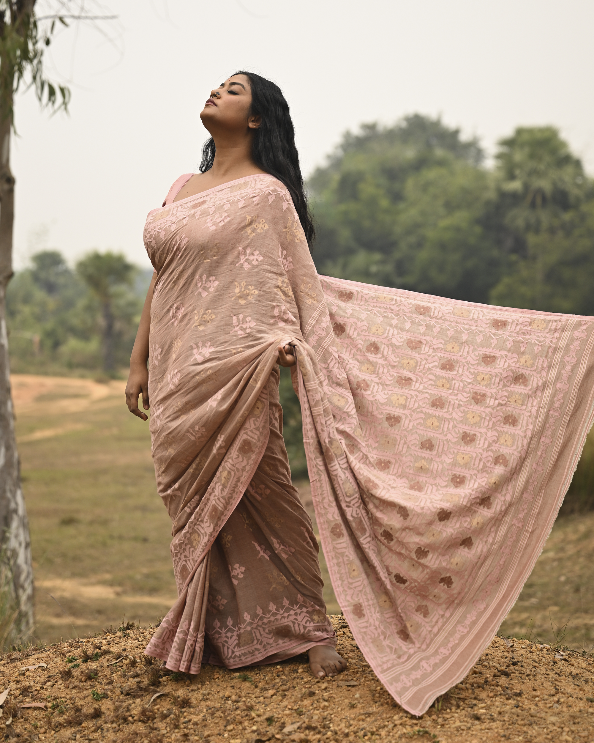 Model wearing the Blush Nude Pastel Jamdani Saree, a handwoven blush nude with pastel rose and muted gold weave Jamdani saree with rich woven body and border work with soft pastel accents and heavily detailed pallu made to be worn open.