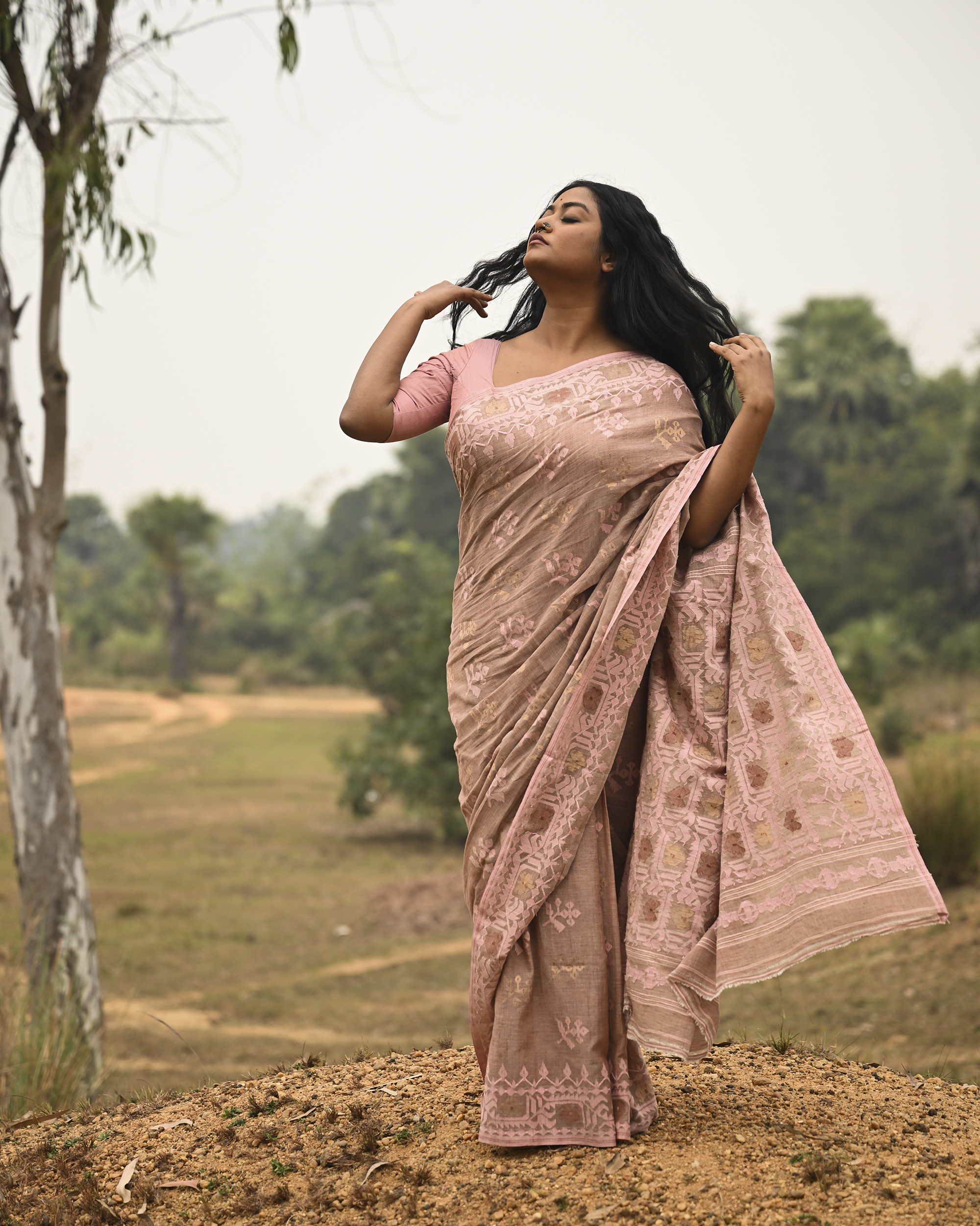 Model wearing the Blush Nude Pastel Jamdani Saree, a handwoven blush nude with pastel rose and muted gold weave Jamdani saree with rich woven body and border work with soft pastel accents and heavily detailed pallu made to be worn open.