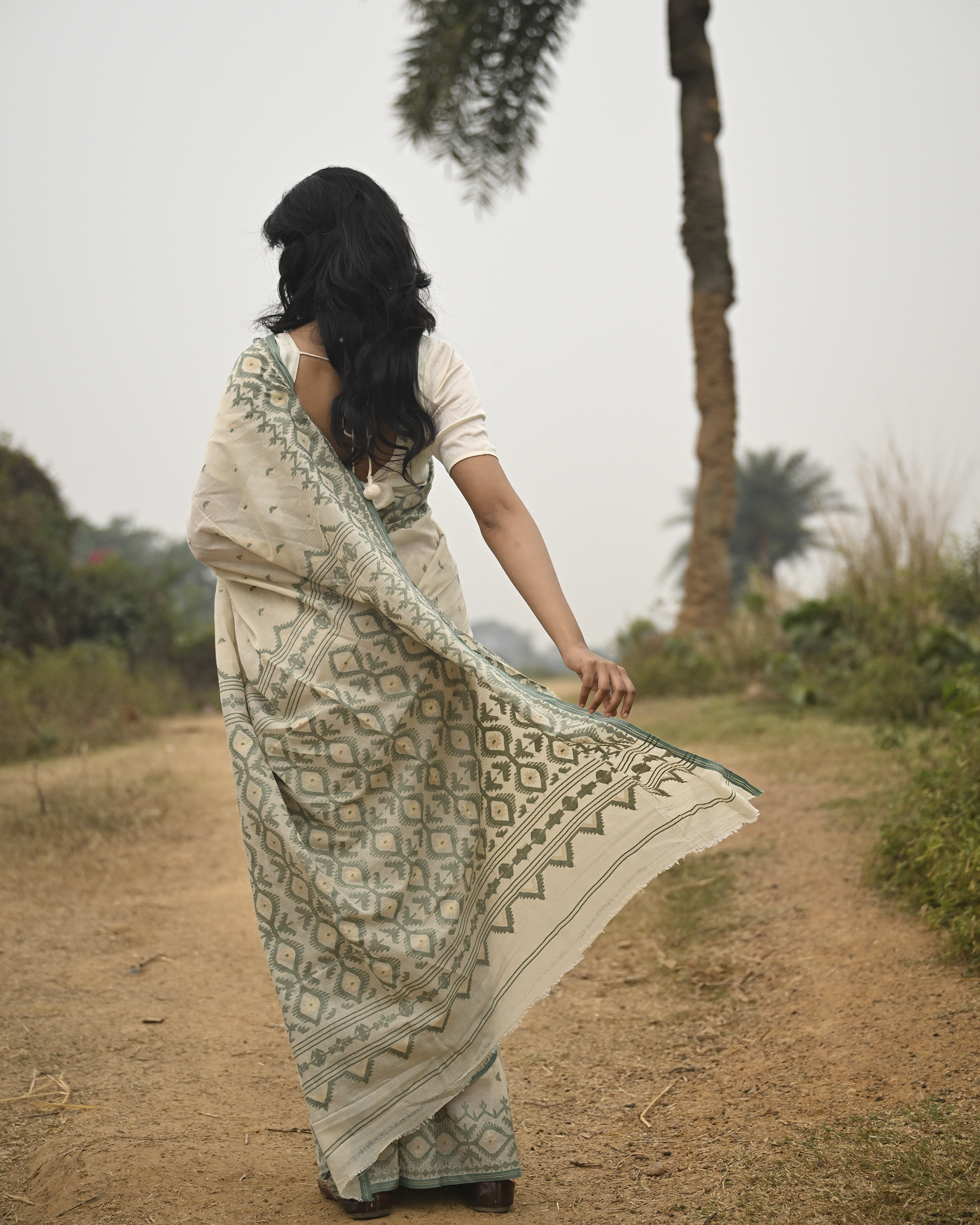 Model wearing the Ivory Sage Pallu Jamdani Saree, a handwoven soft ivory with sage-green edging Jamdani saree with subtle body motifs with architectural woven detailing and beautifully patterned pallu edged in sage-green weaving.