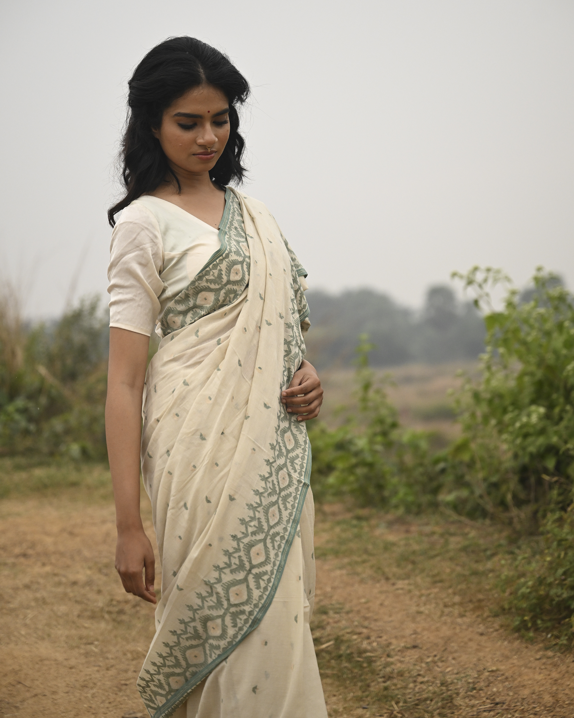 Model wearing the Ivory Sage Pallu Jamdani Saree, a handwoven soft ivory with sage-green edging Jamdani saree with subtle body motifs with architectural woven detailing and beautifully patterned pallu edged in sage-green weaving.