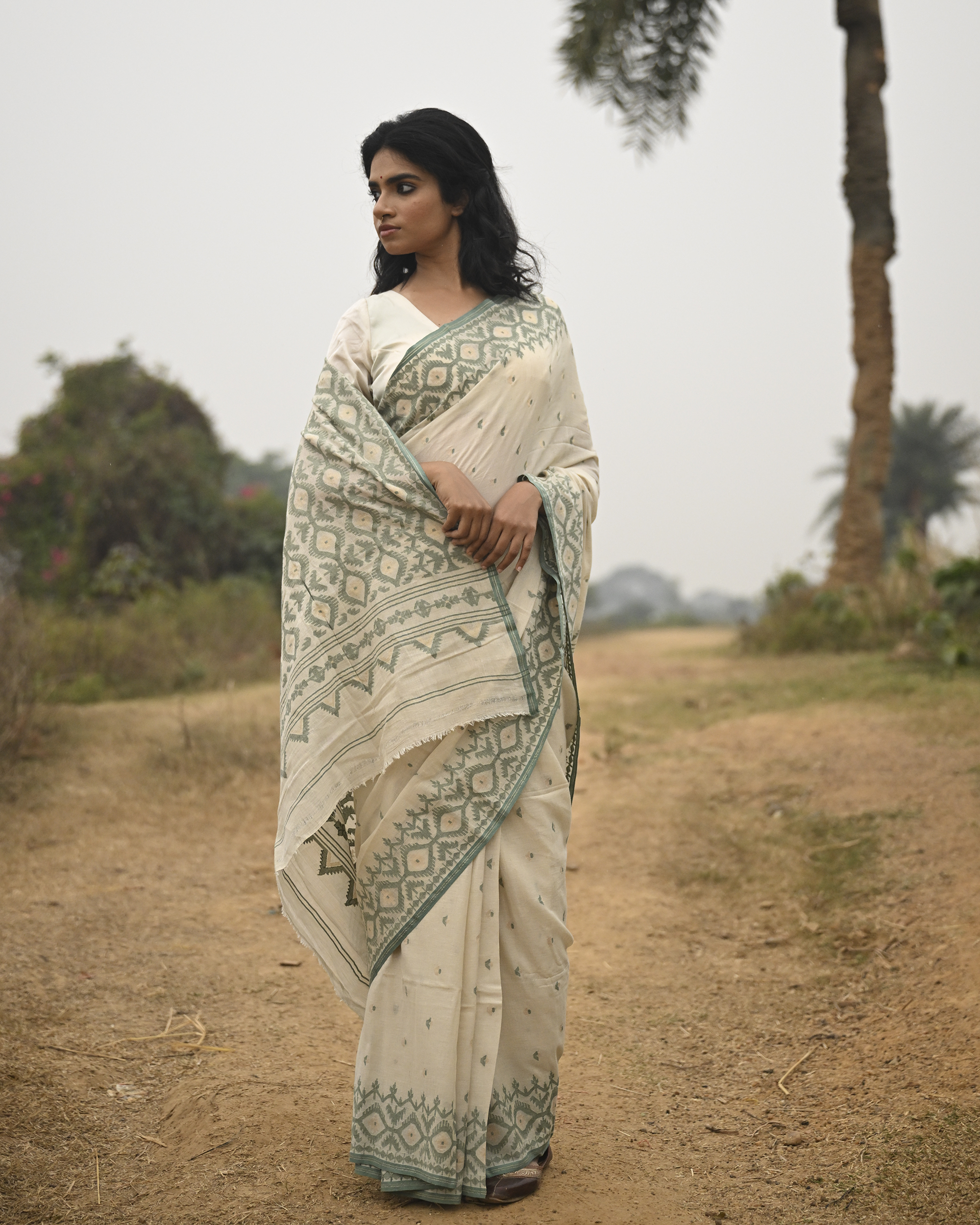 Model wearing the Ivory Sage Pallu Jamdani Saree, a handwoven soft ivory with sage-green edging Jamdani saree with subtle body motifs with architectural woven detailing and beautifully patterned pallu edged in sage-green weaving.