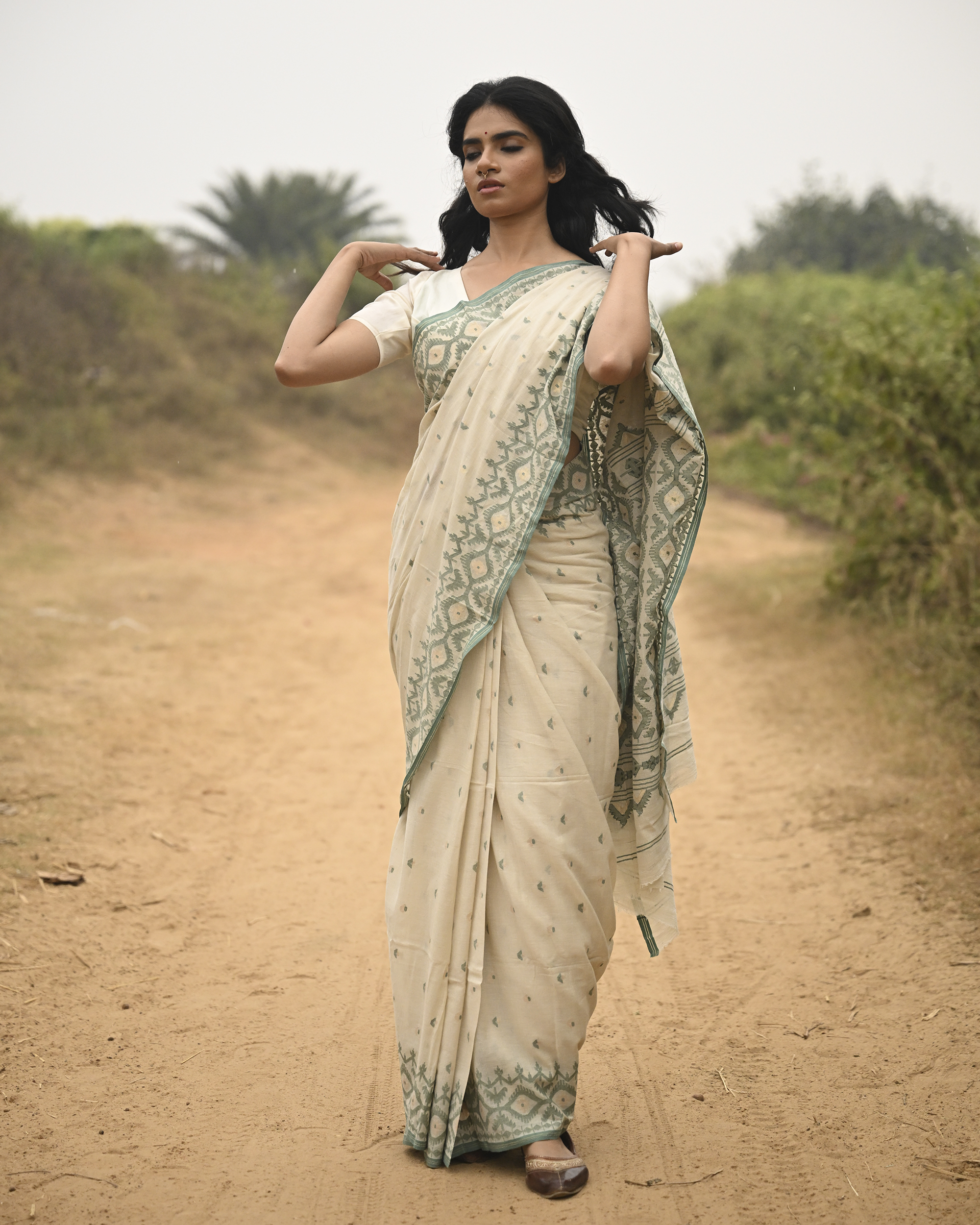 Model wearing the Ivory Sage Pallu Jamdani Saree, a handwoven soft ivory with sage-green edging Jamdani saree with subtle body motifs with architectural woven detailing and beautifully patterned pallu edged in sage-green weaving.