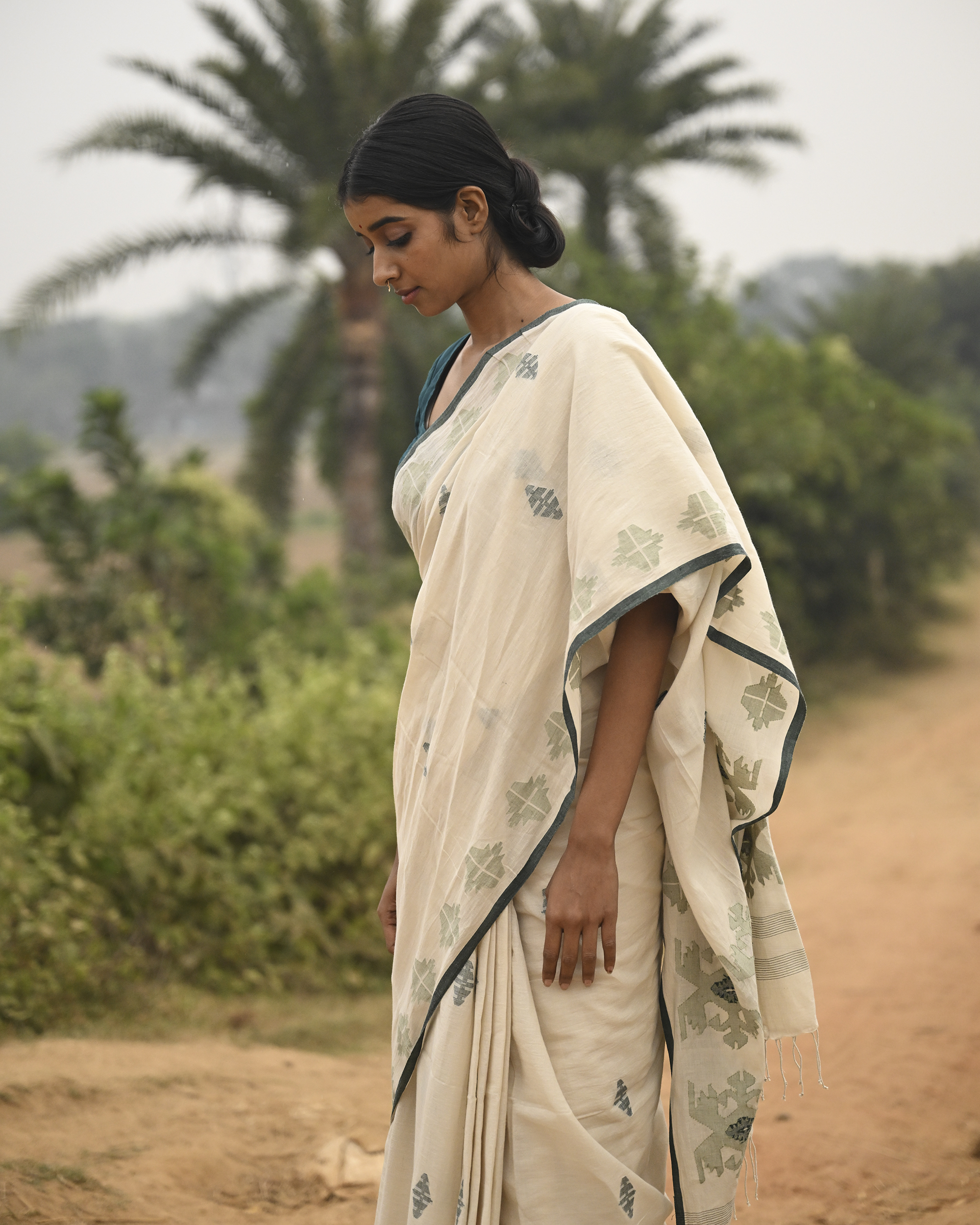 Model wearing the Off-White Sage Buti Jamdani Saree, a handwoven off-white with sage-green motifs Jamdani saree with delicate sage butis across a restrained body and delicately worked anchal with soft green highlights.