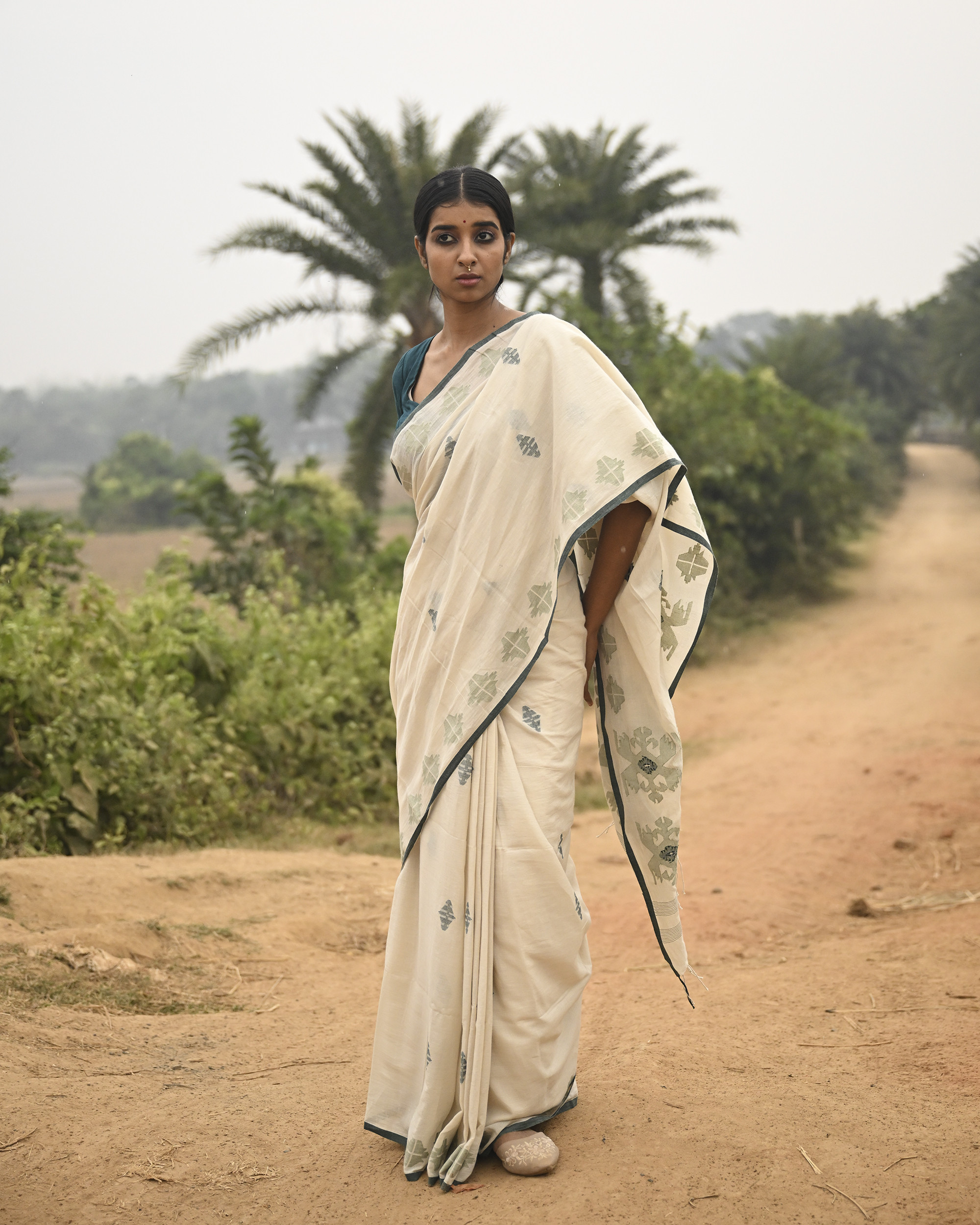 Model wearing the Off-White Sage Buti Jamdani Saree, a handwoven off-white with sage-green motifs Jamdani saree with delicate sage butis across a restrained body and delicately worked anchal with soft green highlights.