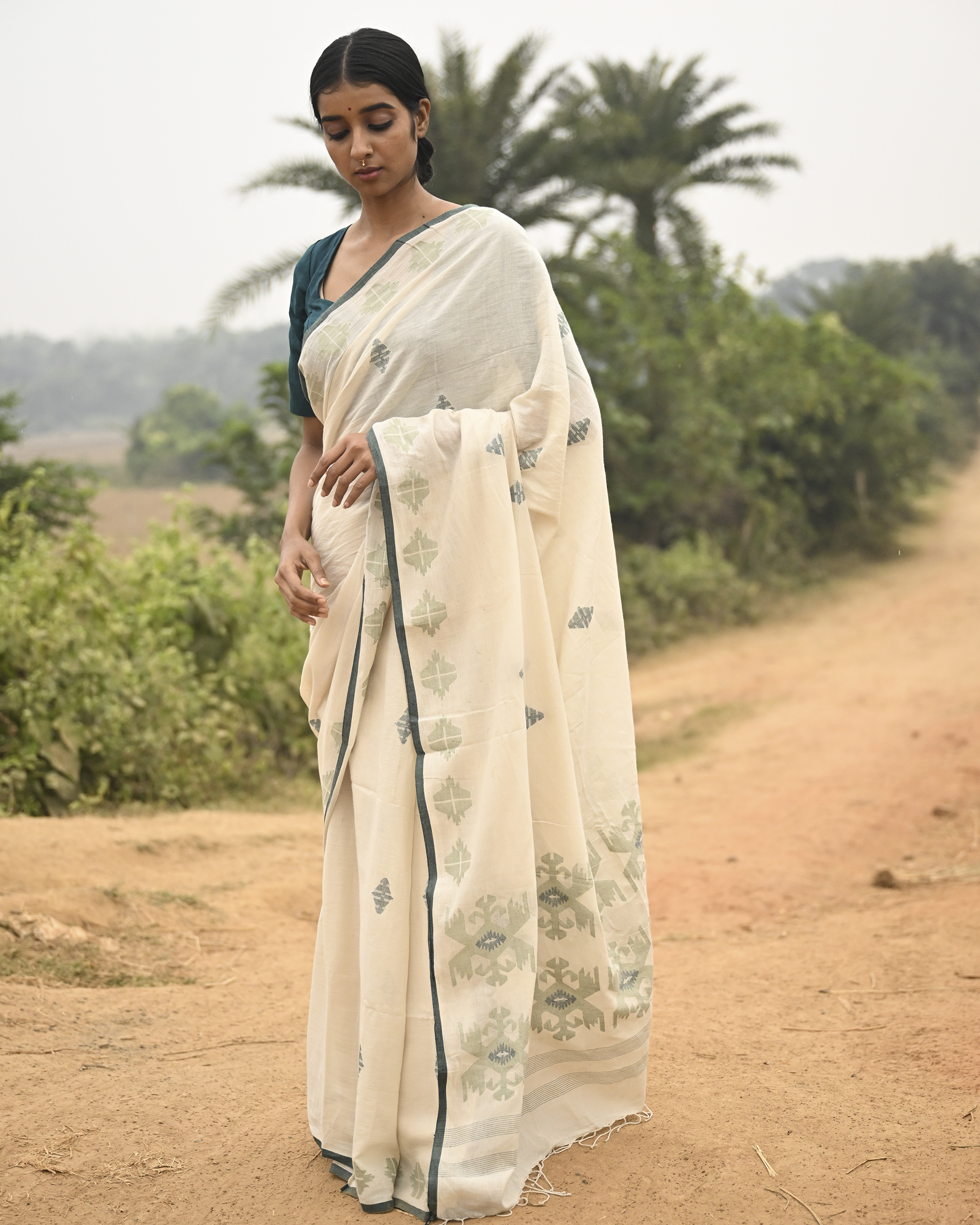 Model wearing the Off-White Sage Buti Jamdani Saree, a handwoven off-white with sage-green motifs Jamdani saree with delicate sage butis across a restrained body and delicately worked anchal with soft green highlights.